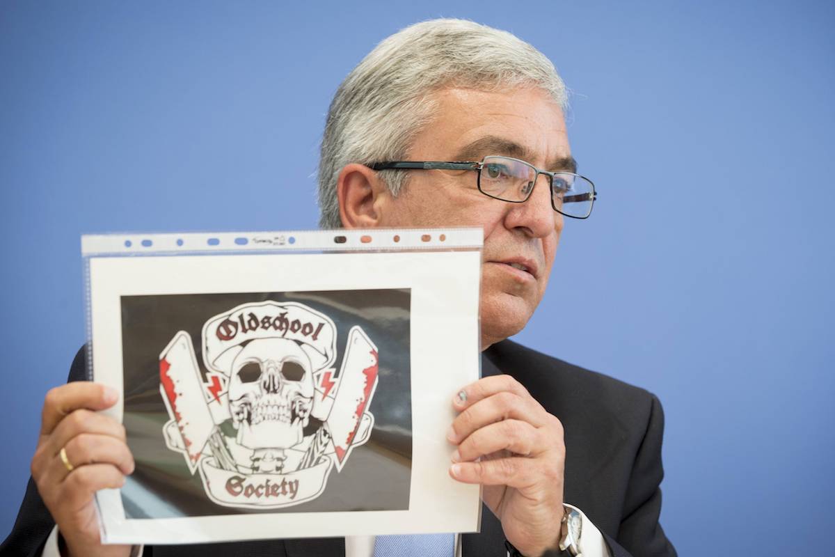 Roger Lewentz, Vorsitzende der Innenminister-Konferenz, zeigt auf einer Pressekonferenz das Logo der Oldschool Society.