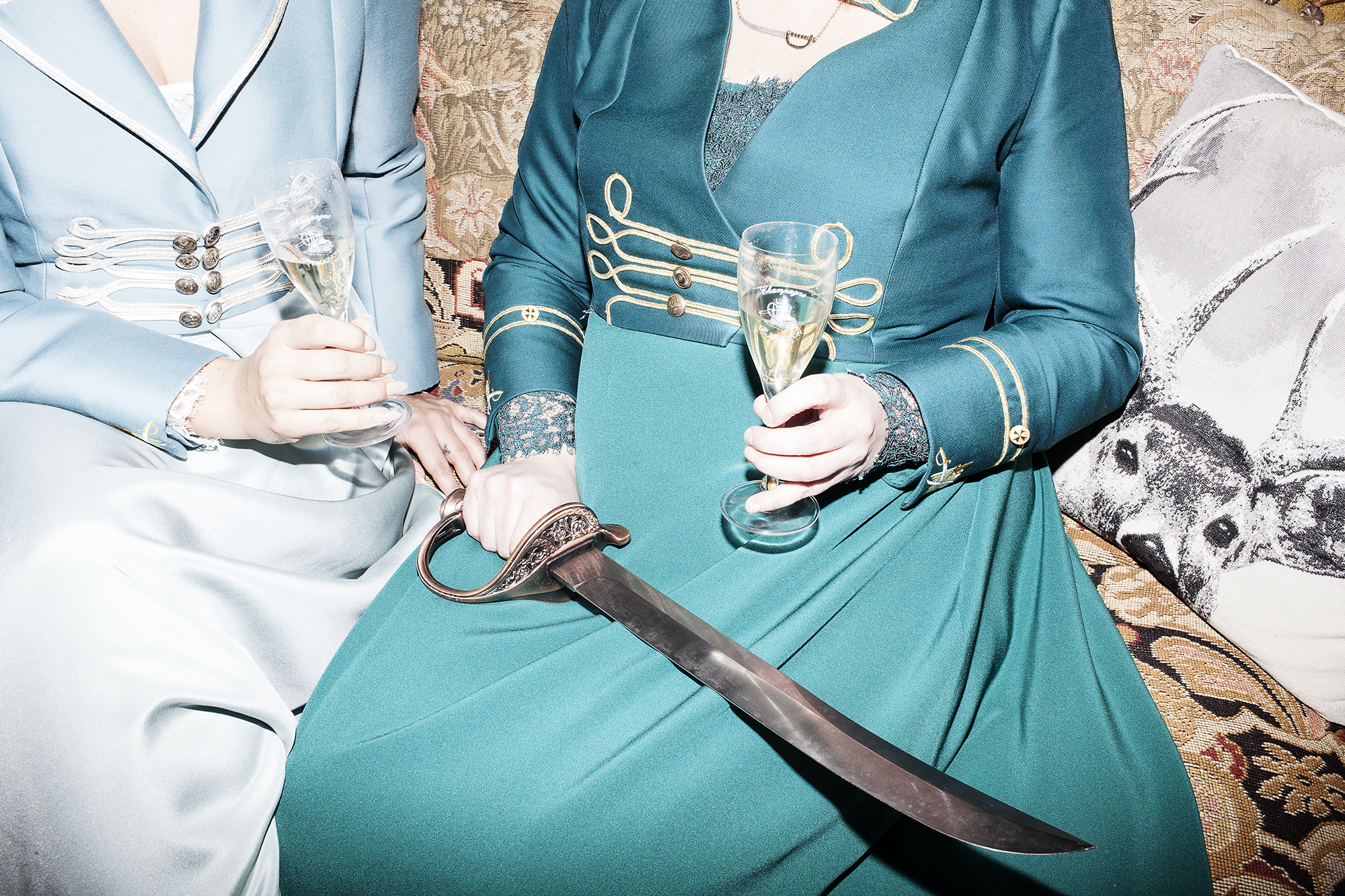 Henriette og Marianne i sofa med champagne i glasset og sabel på skødet.
