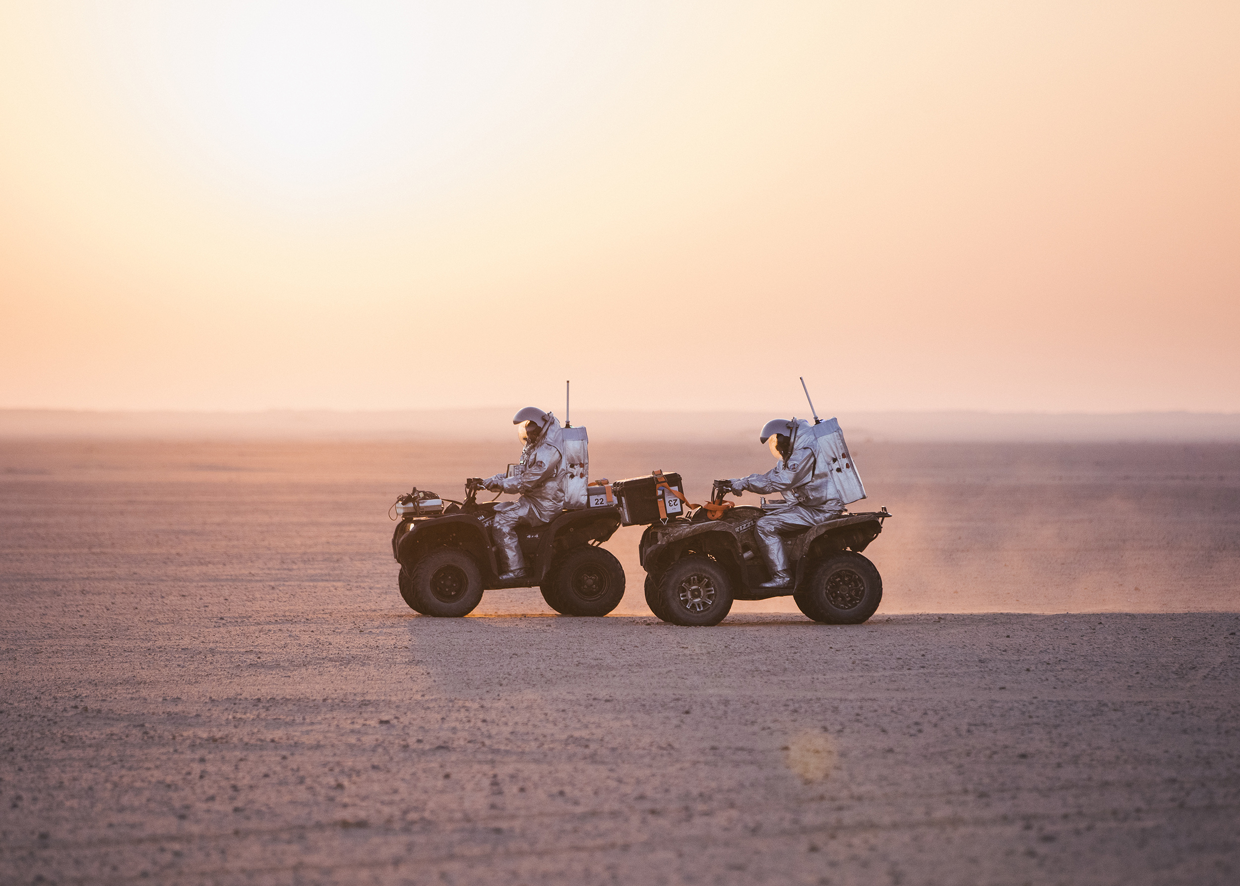 Zwei Analog-Astronauten in Raumanzügen fahren bei Sonnenuntergang auf Quads durch die Wüste von Oman