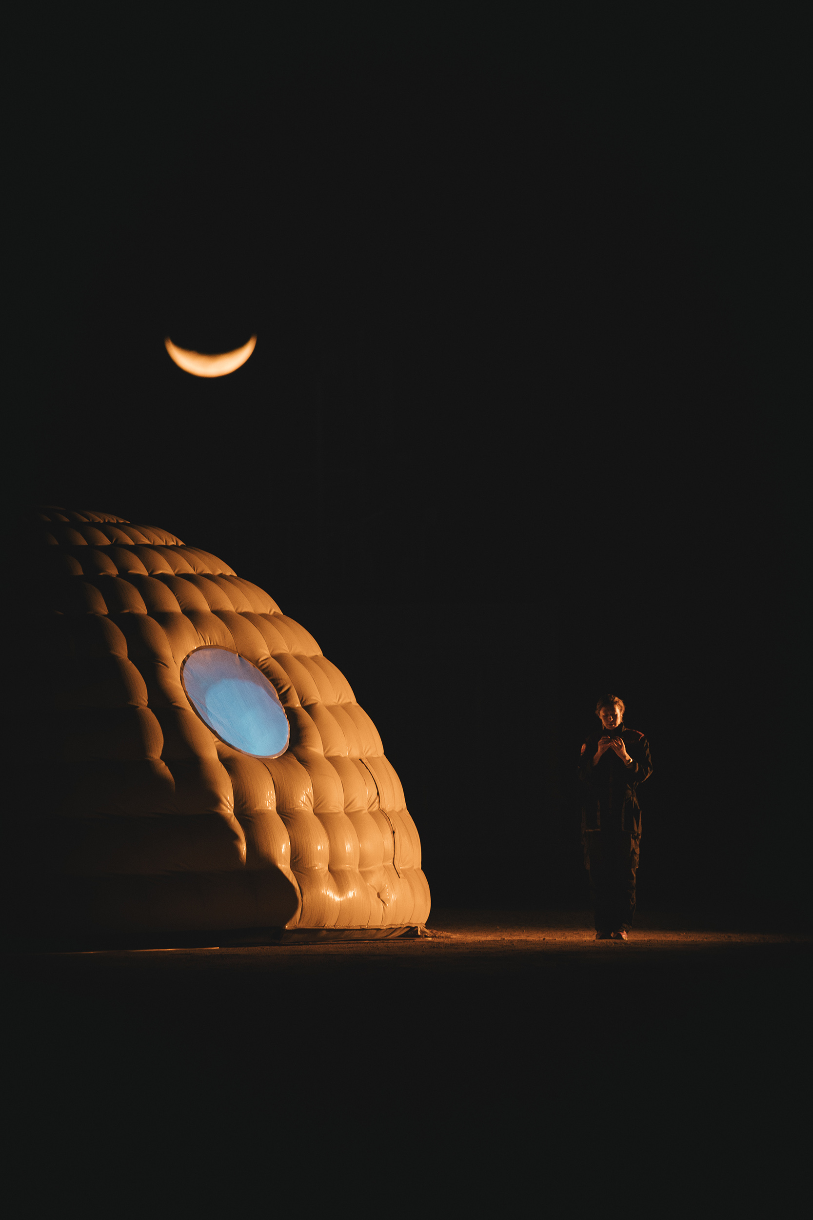 Ein Mensch steht nachts unter einem Sichelmond in der Wüste von Oman, daneben die Kepler Station