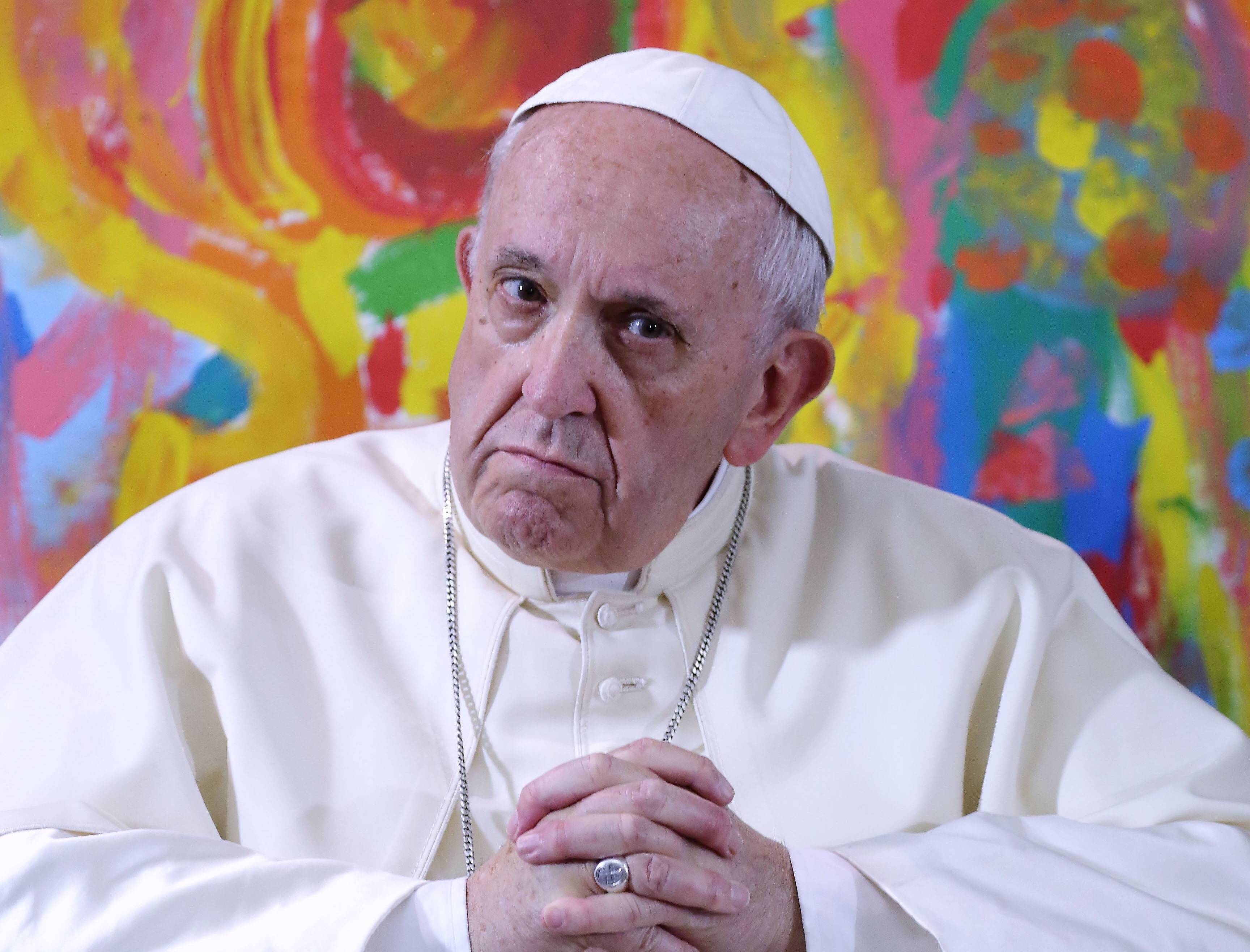 Papst Franziskus schaut gelangweilt vor einer bunten Wand.