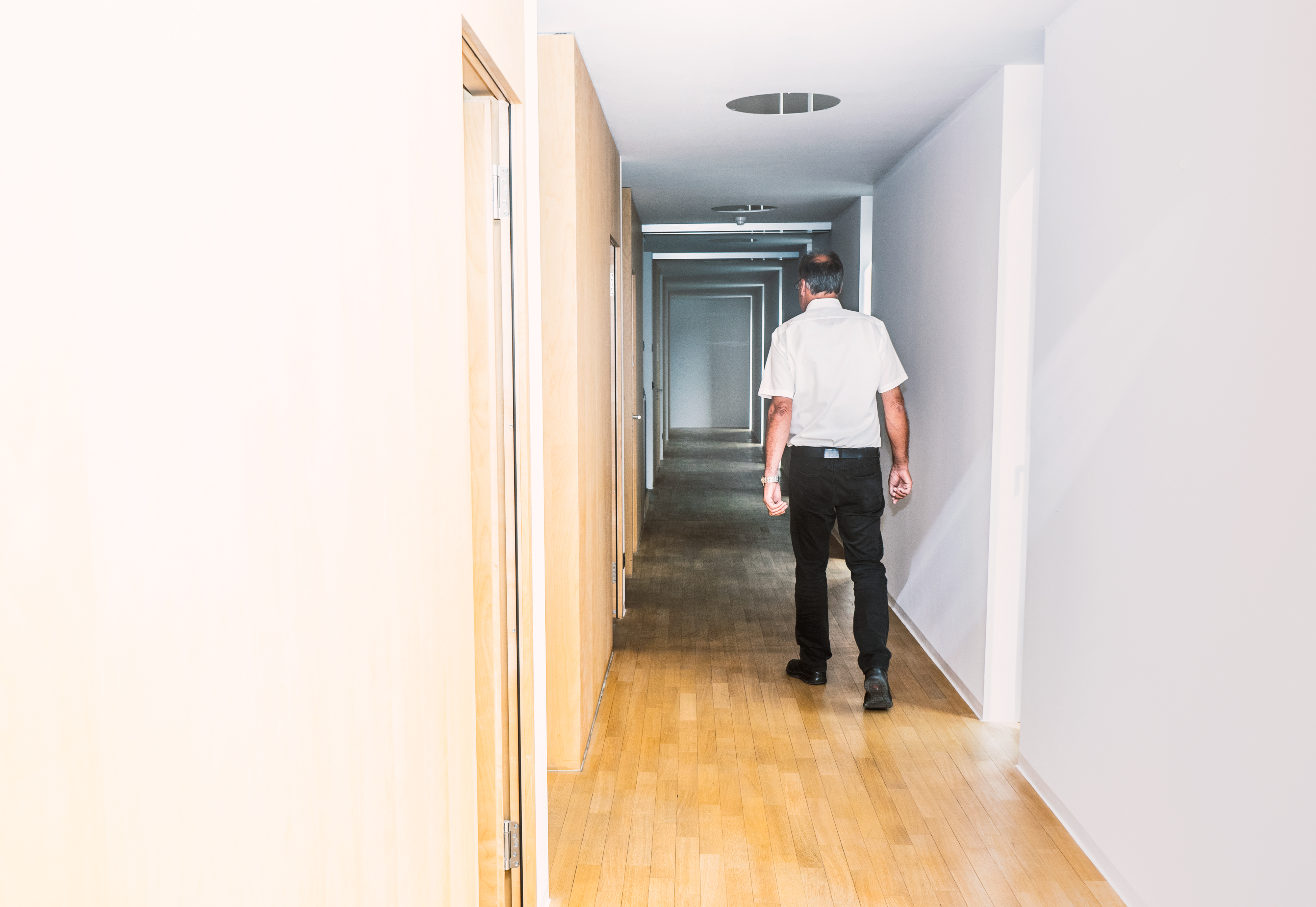 Ein älterer Mann schreitet einen Büroflur entlang