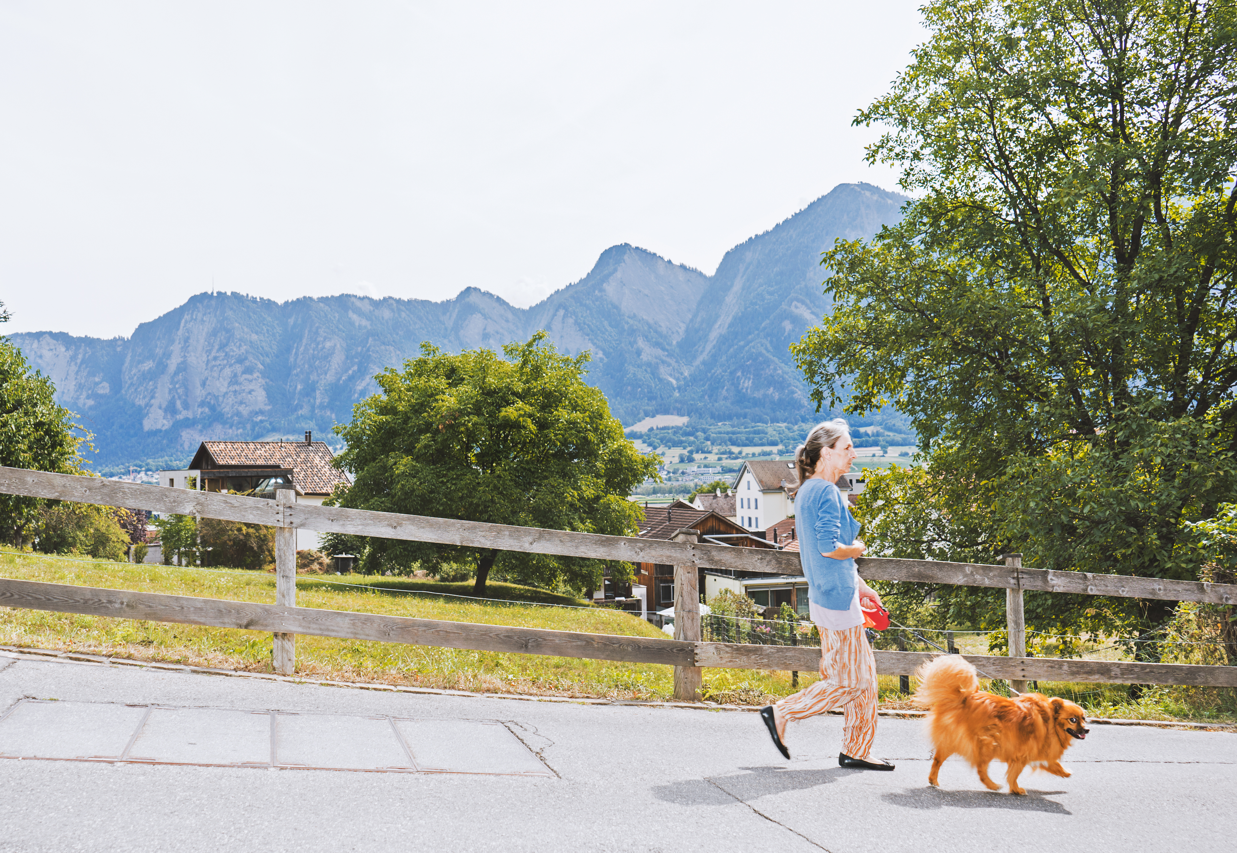 Ein Frau führt ihren Hund Gassi, im Hintergrund erheben sich Berge