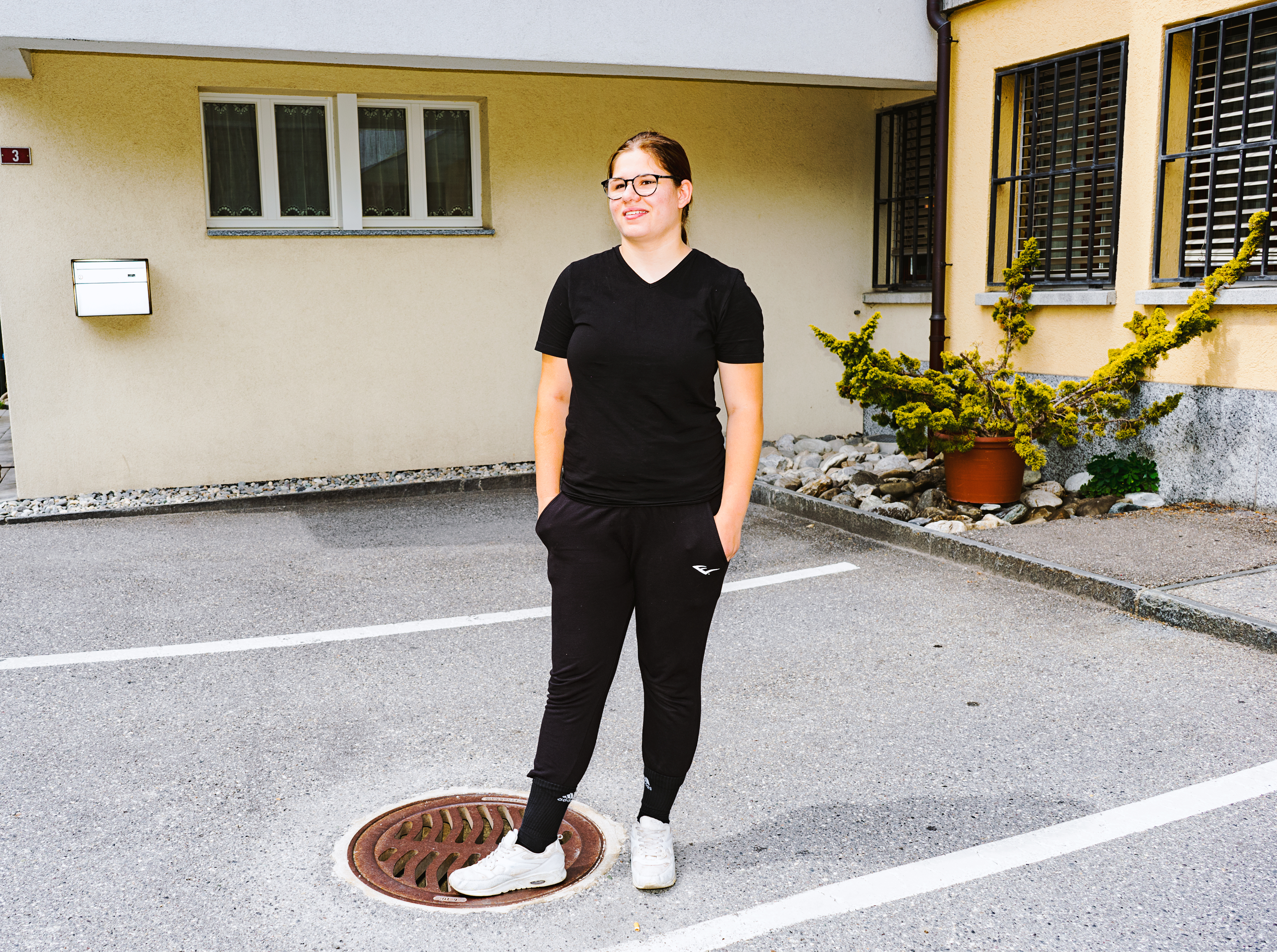 Eine junge Frau steht auf einem Parkplatz, die Hände in den Taschen ihrer Jogginghose