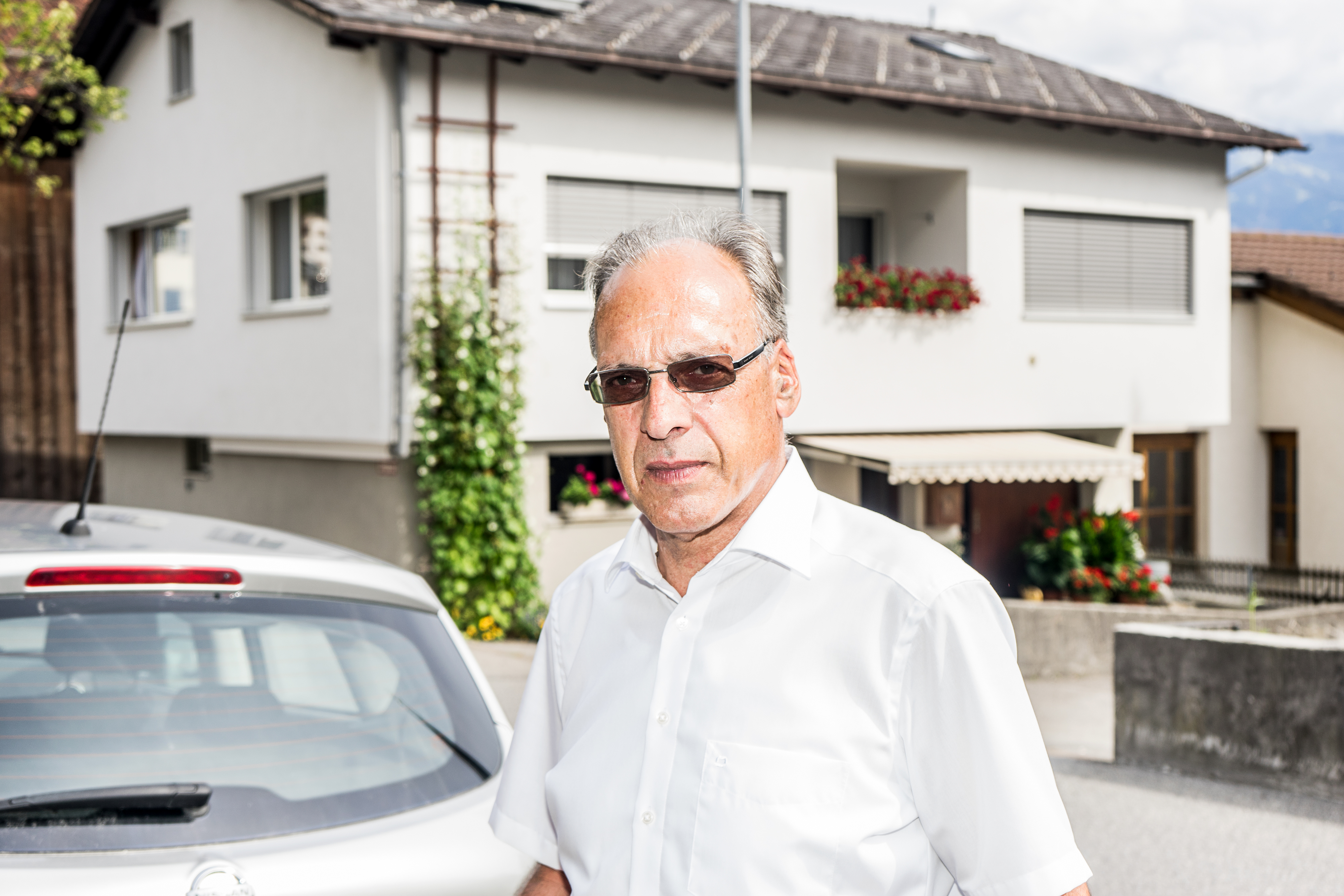 Der Bürgermeister trägt eine Sonnenbrille und steht vor einem Wohnhaus