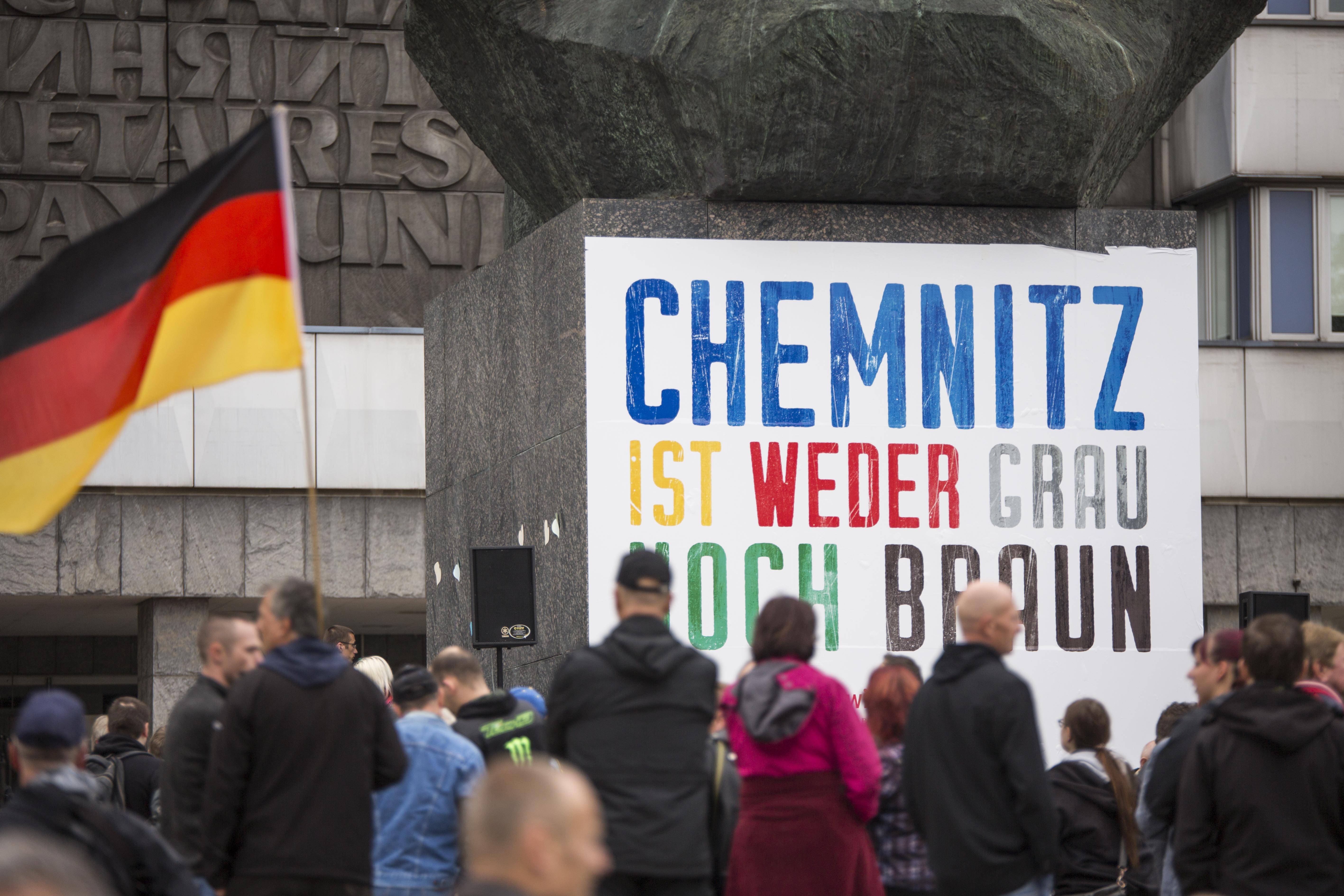 Auf dem Karl-Marx-Monument in Chemnitz klebt ein Plakat, davor versammeln sich Menschen