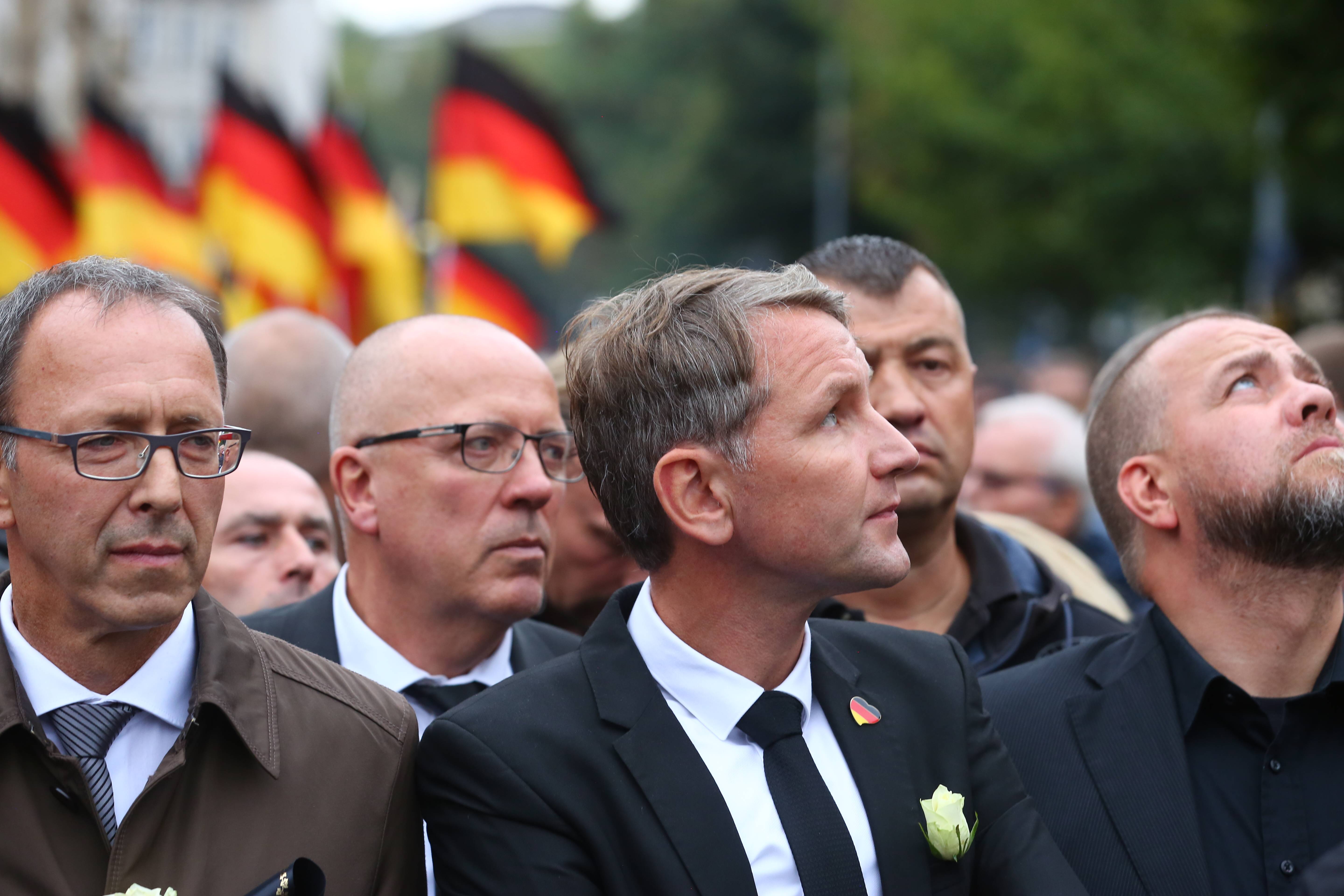 Drei Männer stehen in vorderster Front einer Demonstration, der Mittlere trägt eine weiße Rose