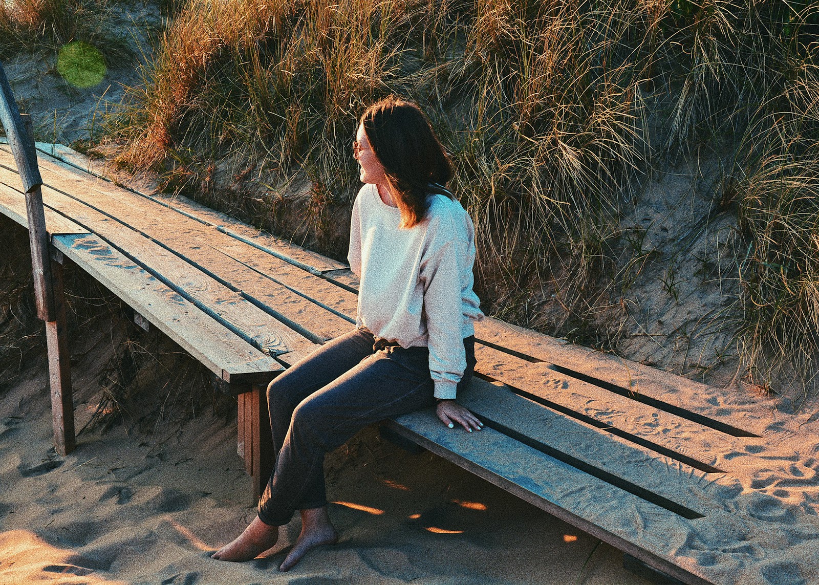 Eine Frau sitzt am Strand und blickt in die Sonne