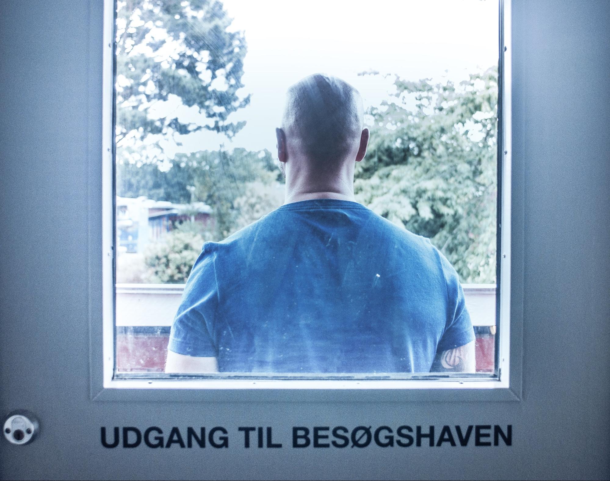 Ein Mann steht in Gefängniskleidung vor einer Tür mit Sichtfenster