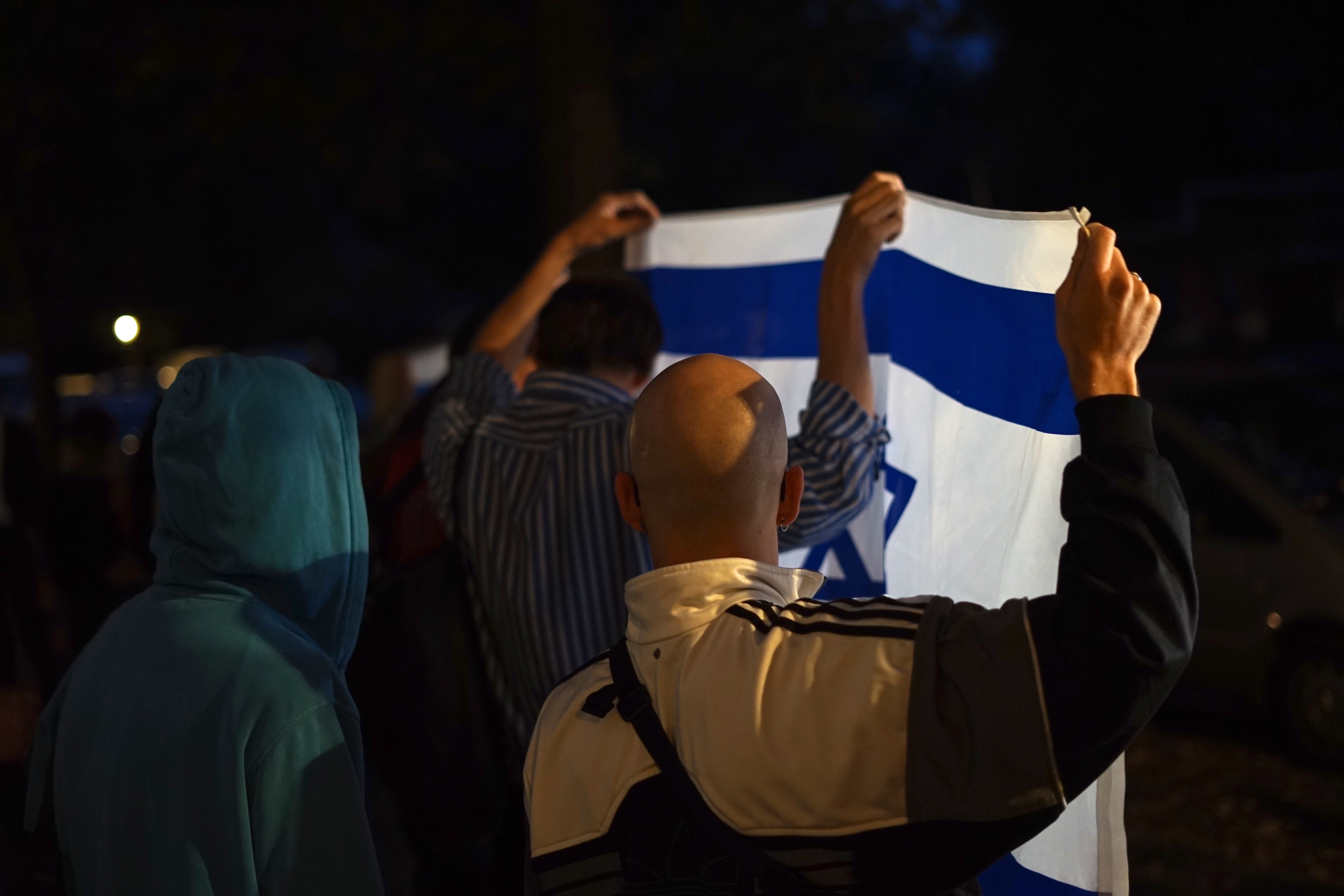 Zwei Männer, den Rücken zur Kamera, halten im Dunklen eine Israel-Fahne hoch