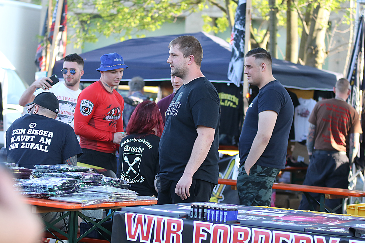 Eine Gruppe von Männer und Frauen an Bierbänken, auf einem T-Shirt steht