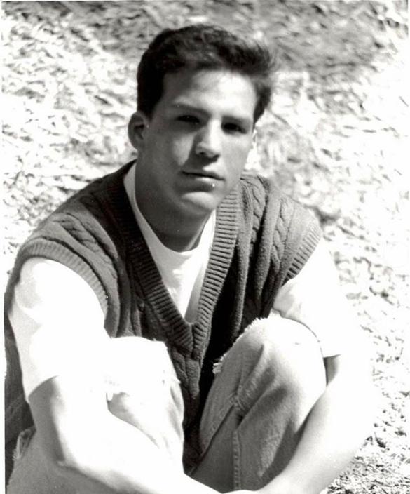 A young man sitting on grass.