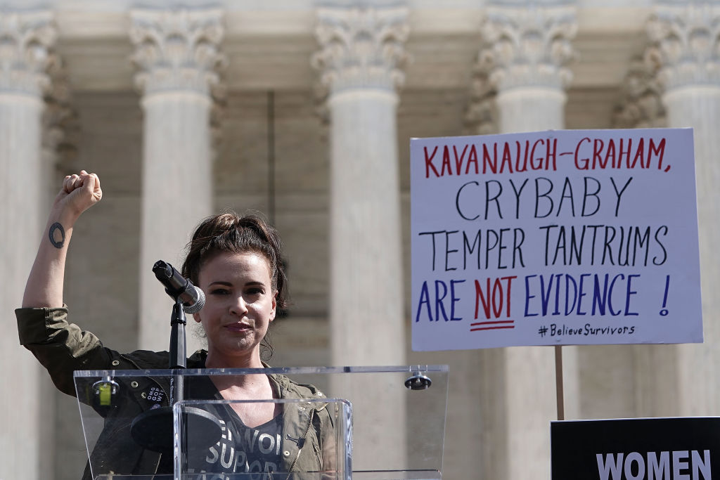 Alyssa Milano standing at a podium in Washington DC with her fist raised.