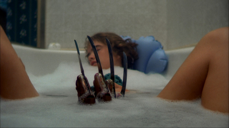 a woman naps in a bathtub while a hand wearing a blade-covered glove rises out of the water between her legs
