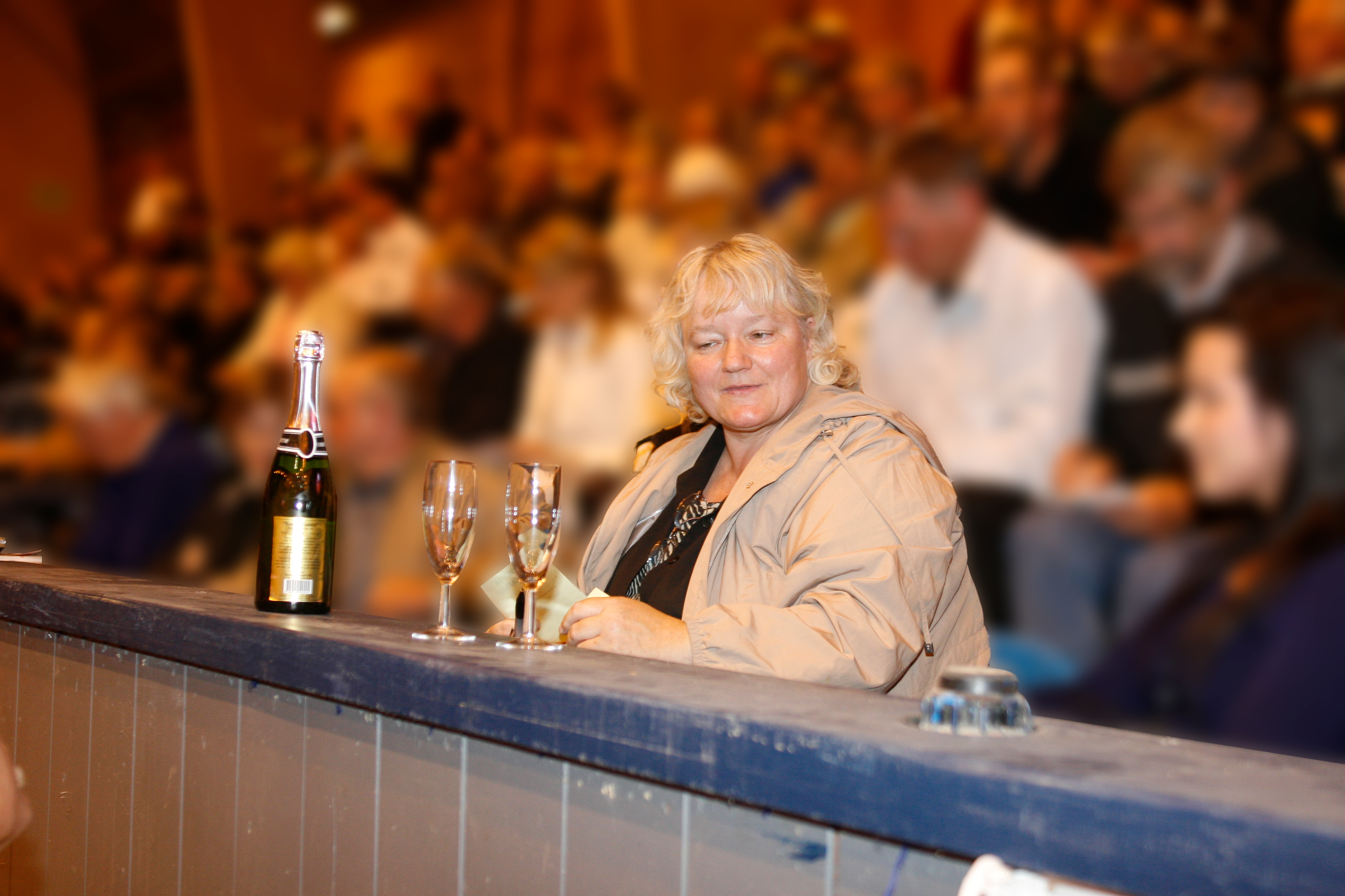 Britta Nielsen sidder ved en bardisk med en flaske champagne og to glas.