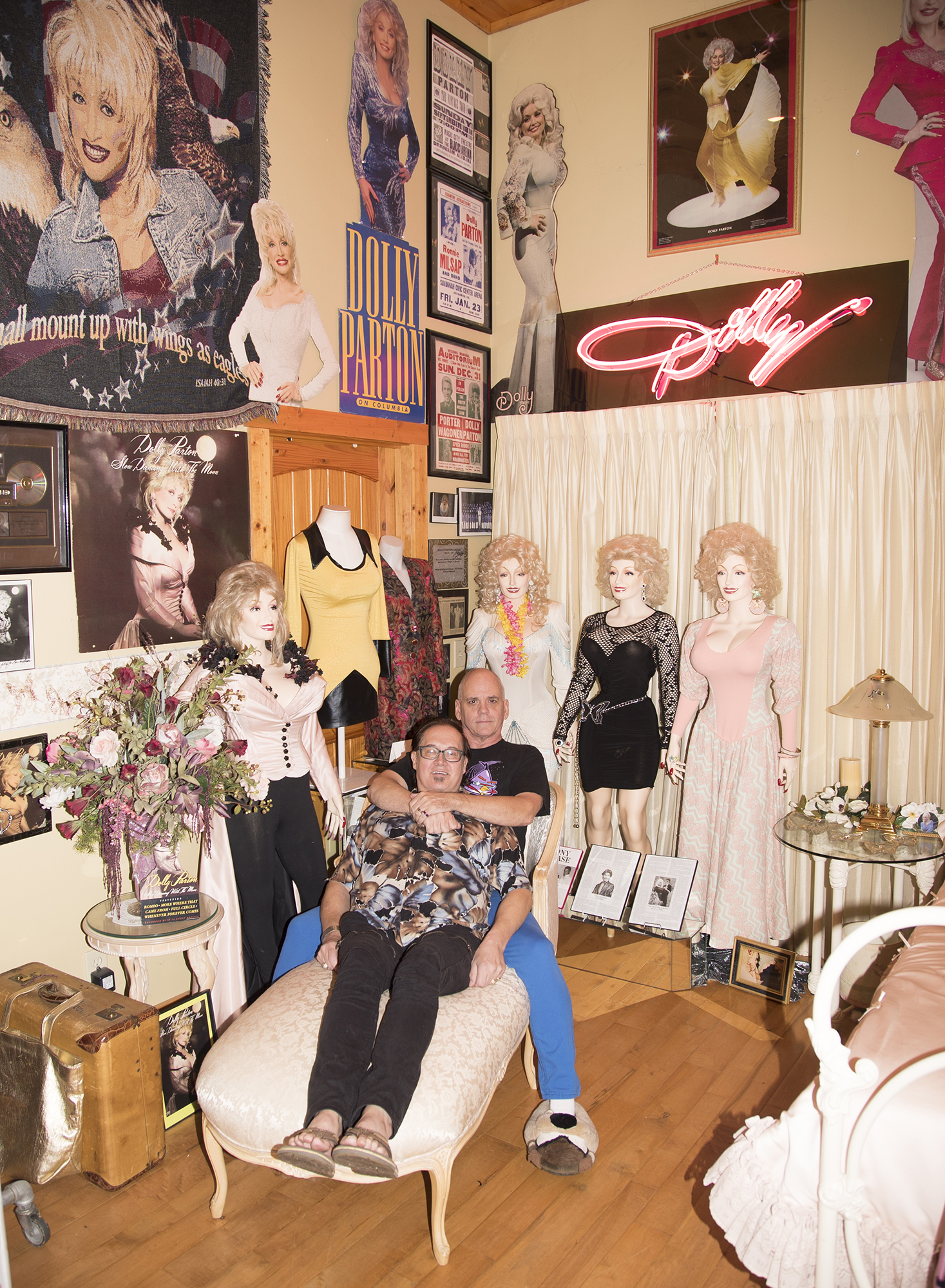 Patric and Harrell sit in front of a section of their Dolly Parton collection, featuring mannequins in Dolly outfits, and framed photos of the singer.