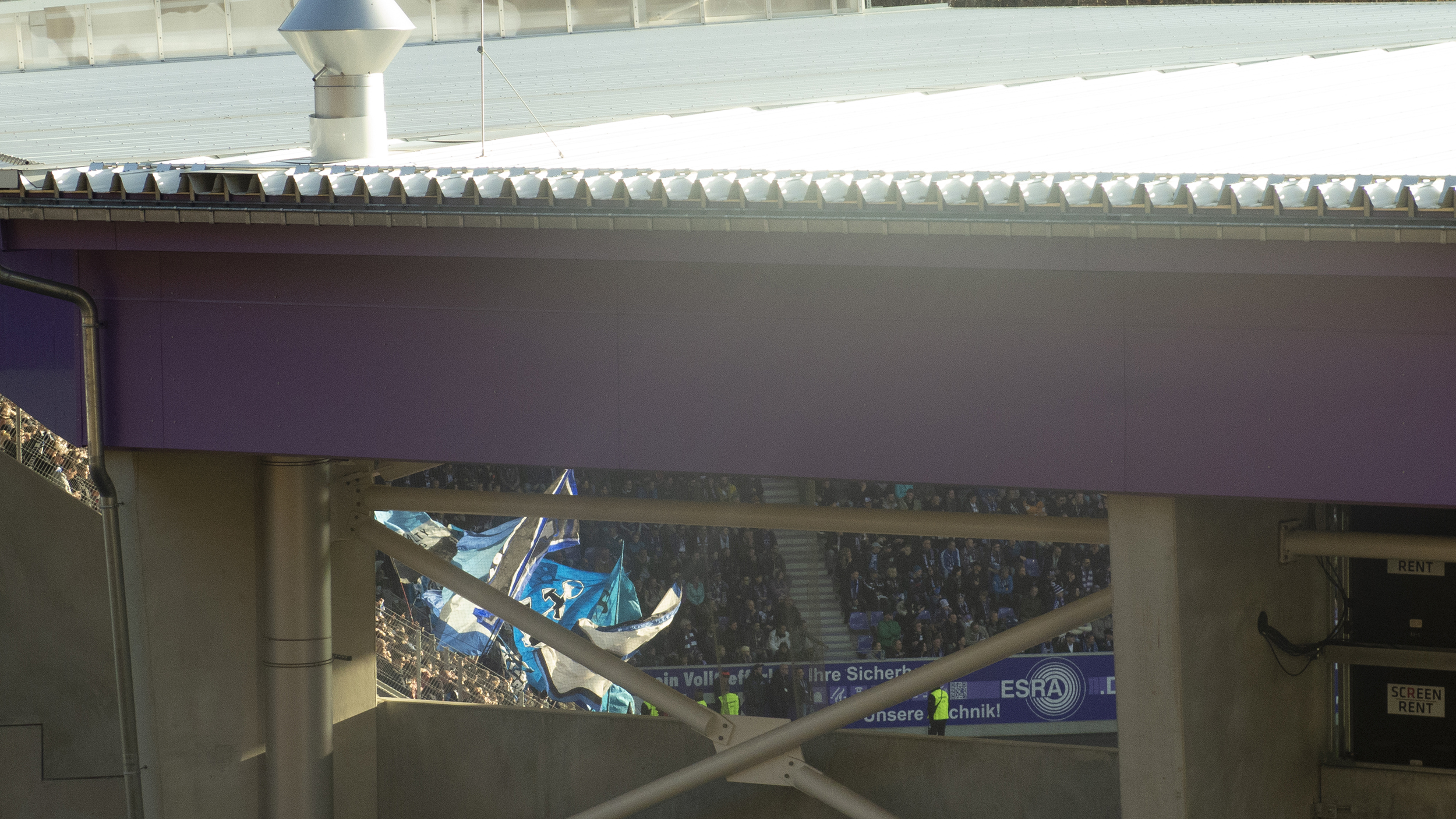 Fans im Stadion, durch eine Lücke im Gebäude fotografiert