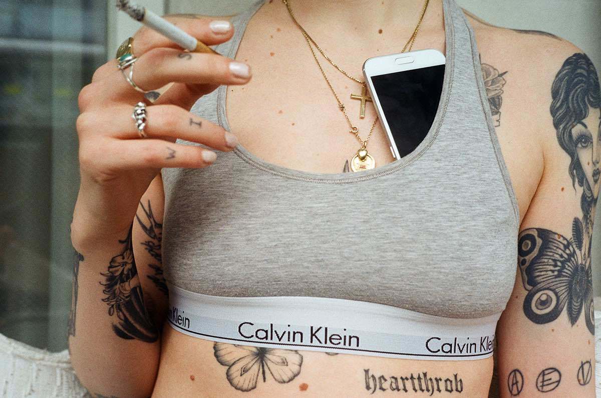 Tattowierte Frau mit Sport-BH, Goldkette und Zigarette.