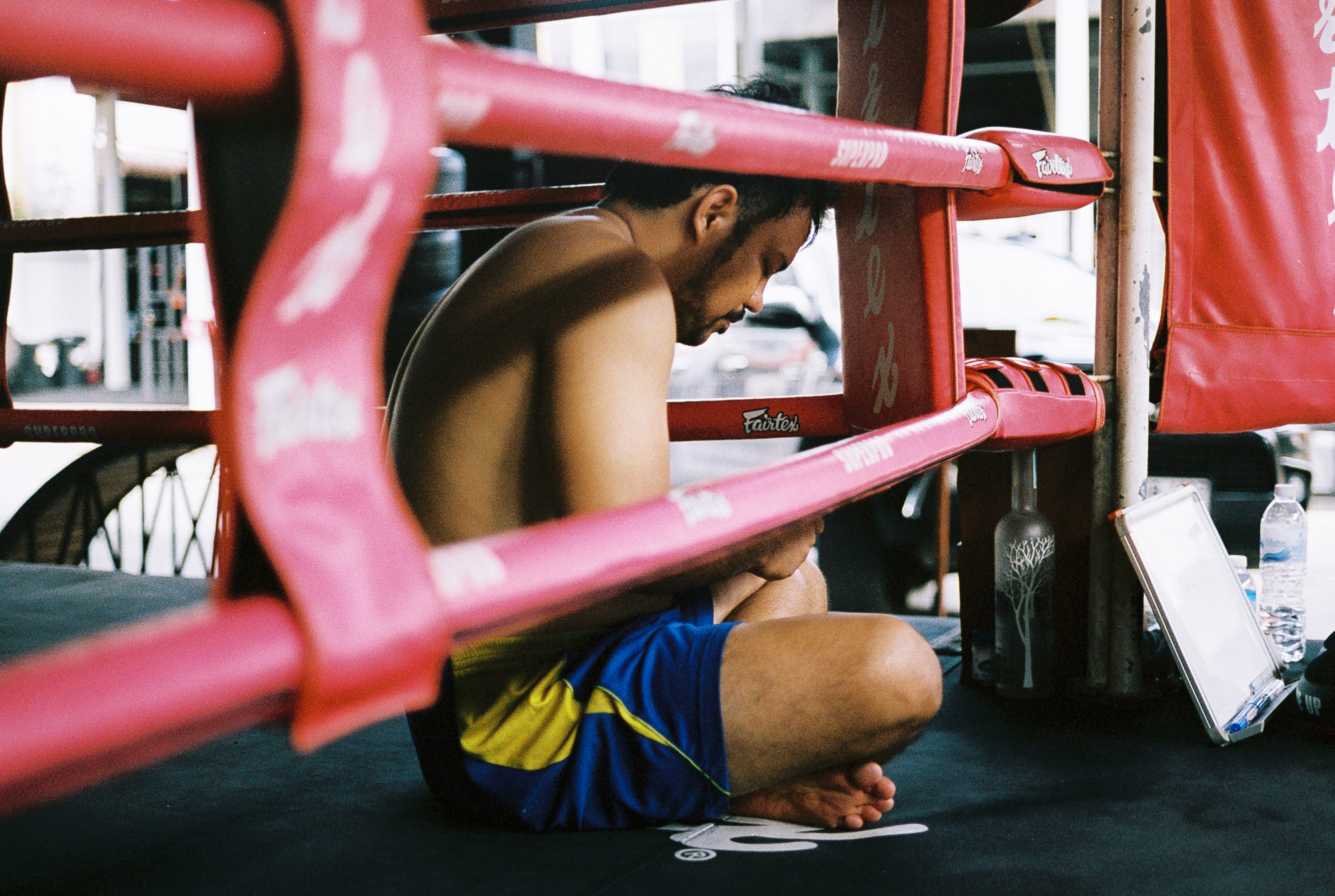Trainer Chai zit in de ring op zijn telefoon, wachtend op de volgende privéles.
