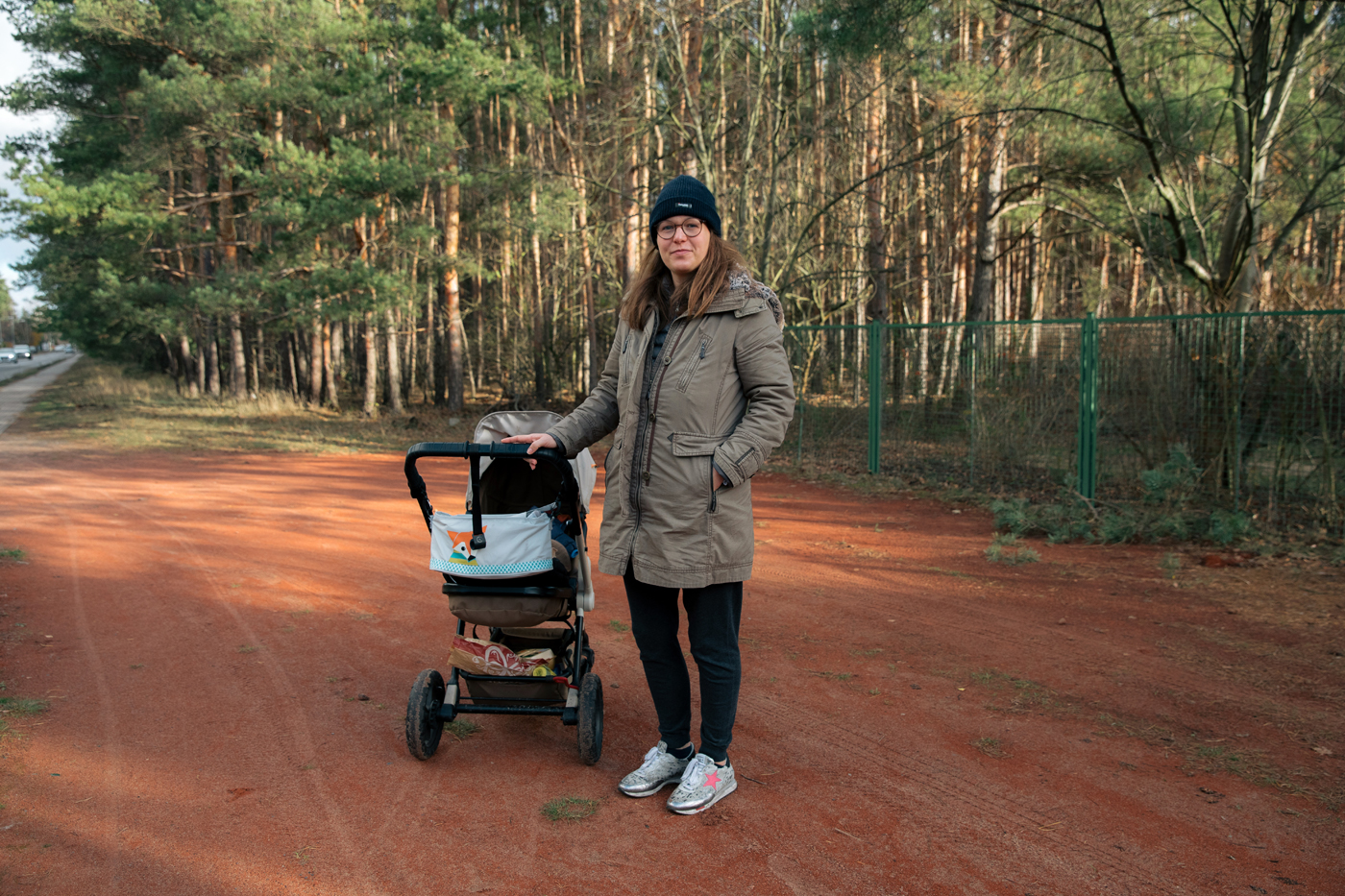 Eine junge Frau mit einem Kinderwagen steht auf einem Weg vor den Kiefern von Müggelheim