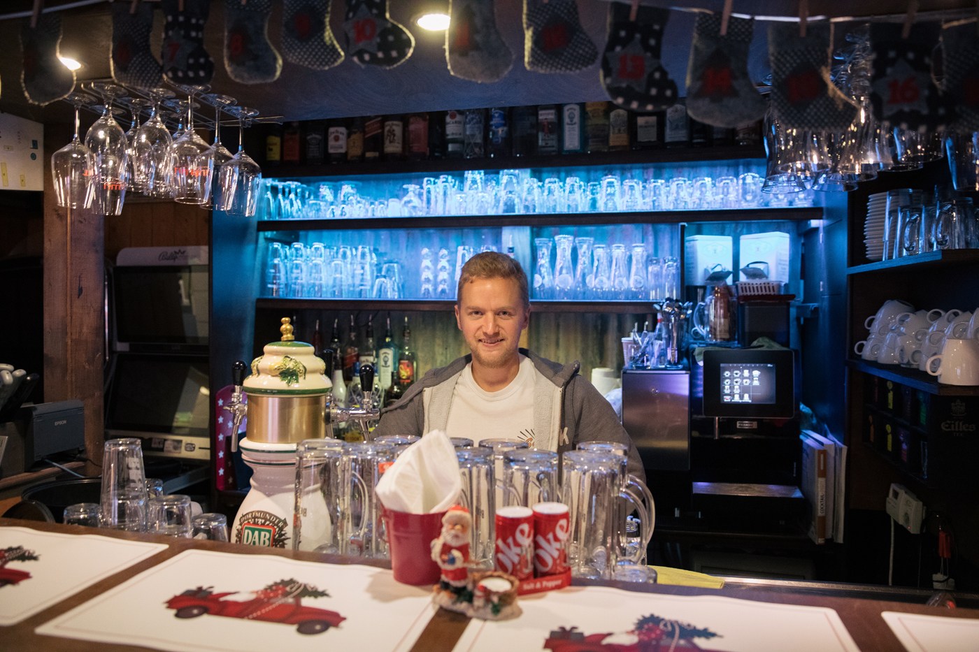 Ein Mann steht hinter der Theke, die Adventskerzen sind Coca-Cola-Dosen nachempfunden