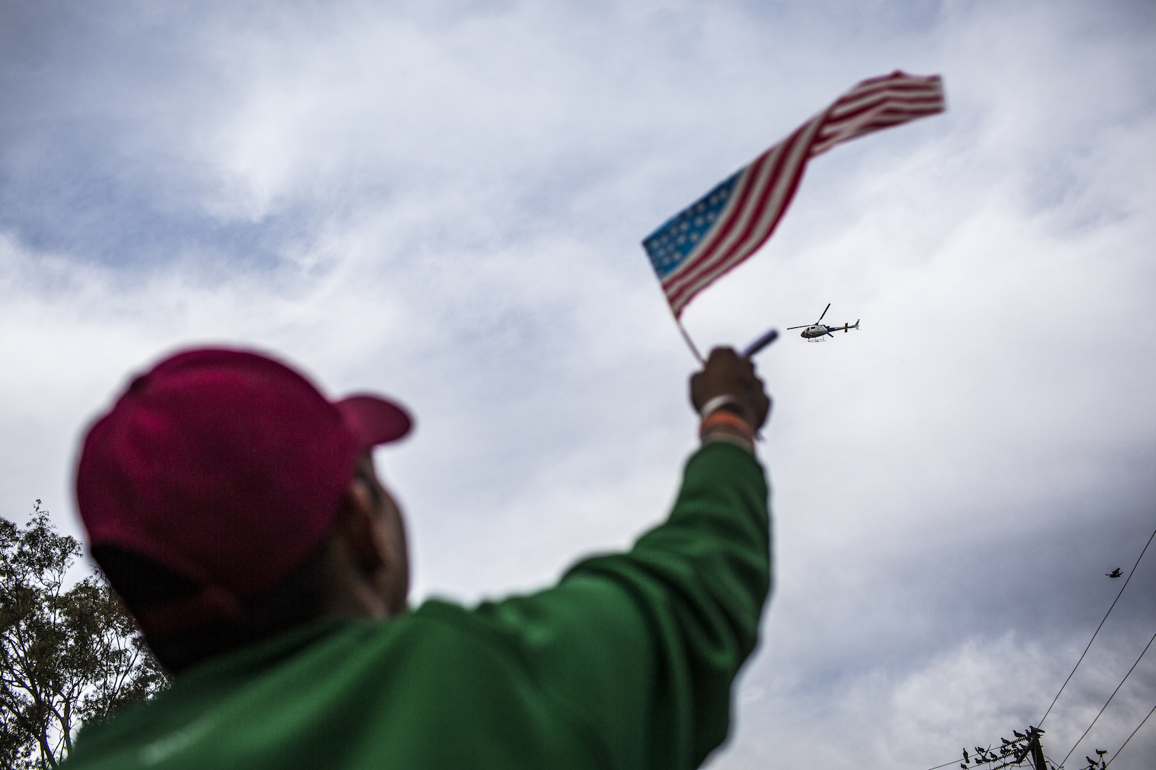 A migrant waves an American flag to a helicopter flying above the migrant shelter just along the U.S.-Mexico border in Tijuana, Mexico. (Jika Gonzales/VICENews).