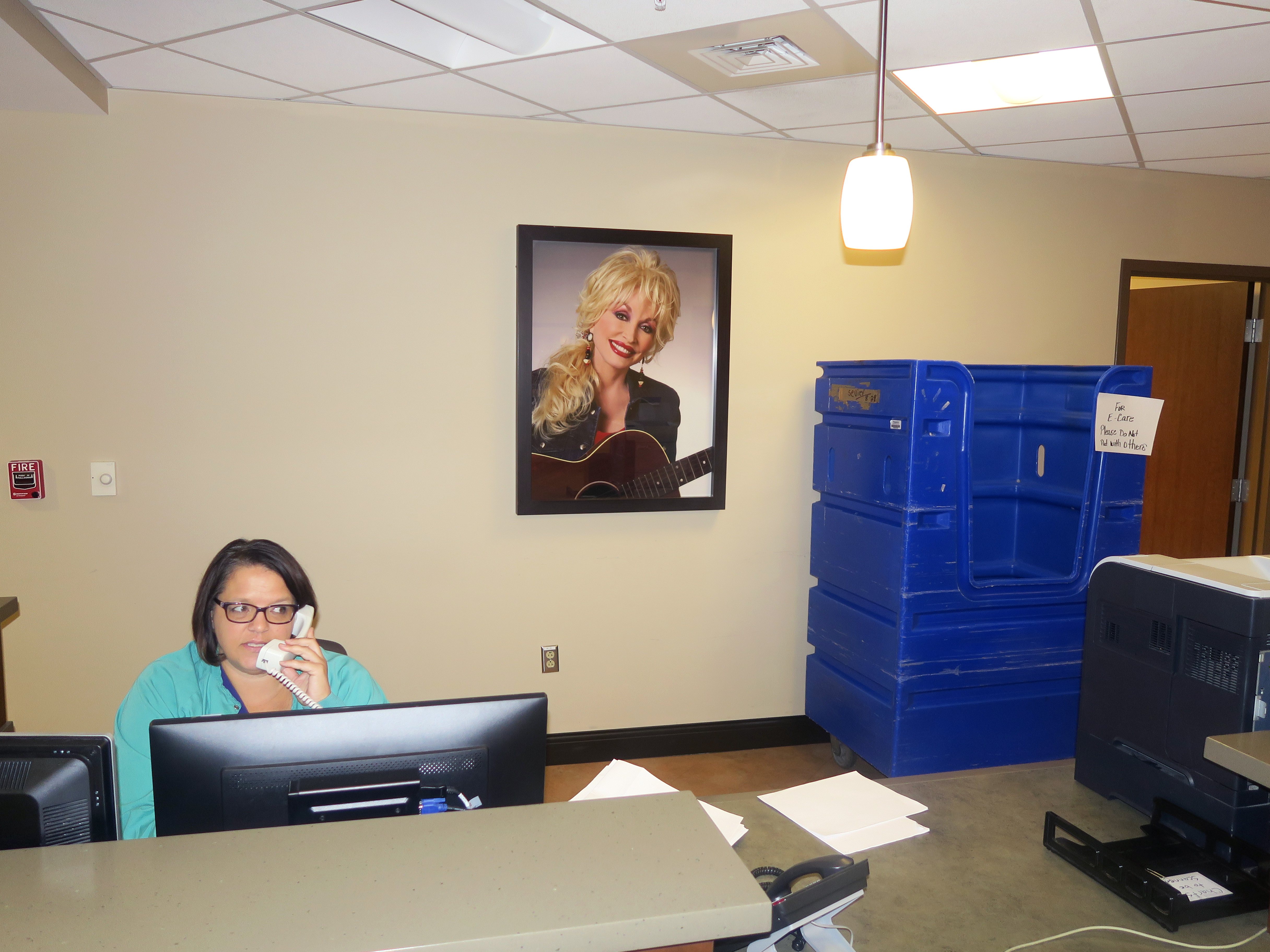 A woman in hospital scrubs answers a phone in front of a portrait of Dolly Parton