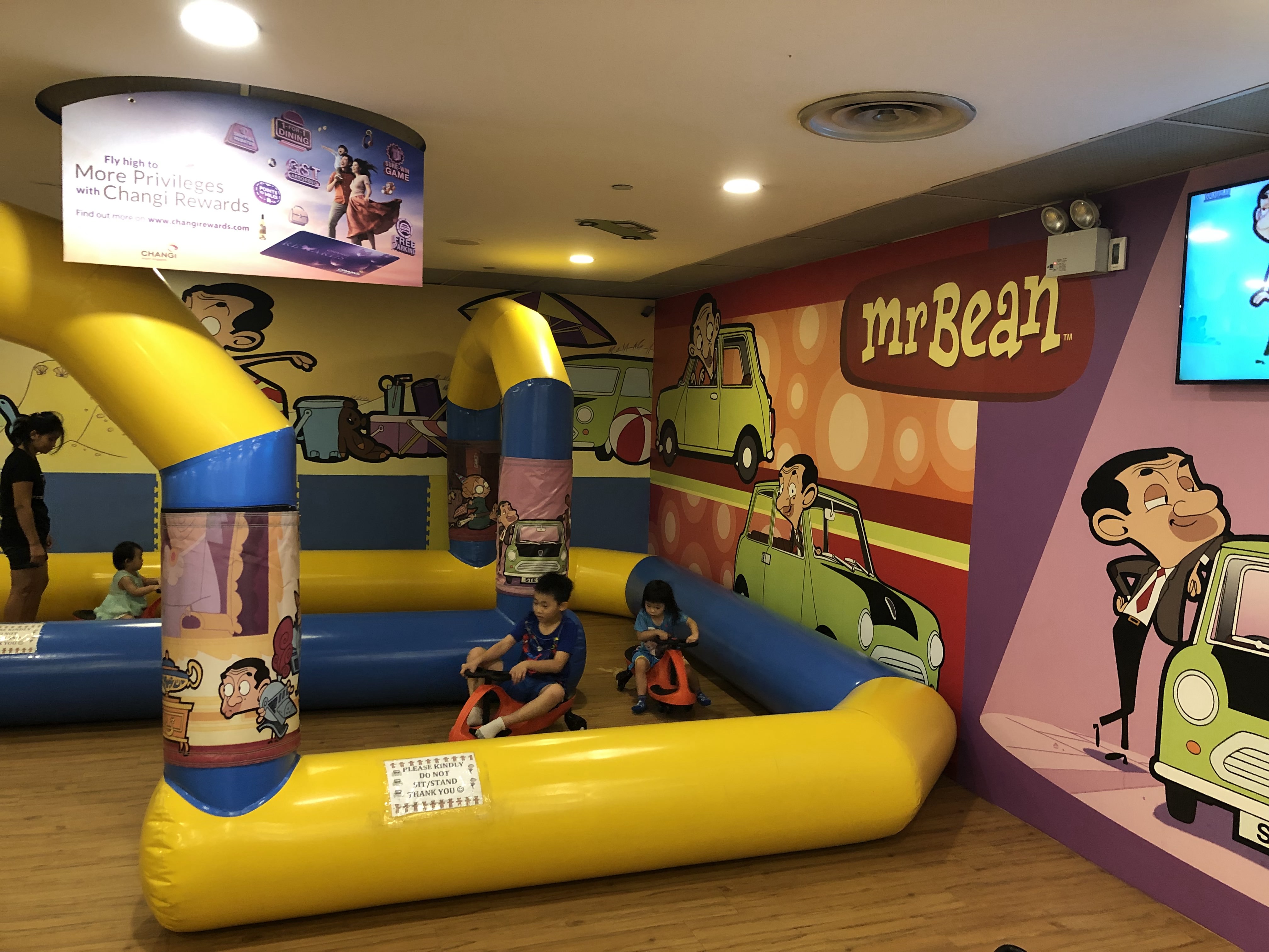 Children drive karts around an inflatable track with Mr. Bean cartoons on the wall