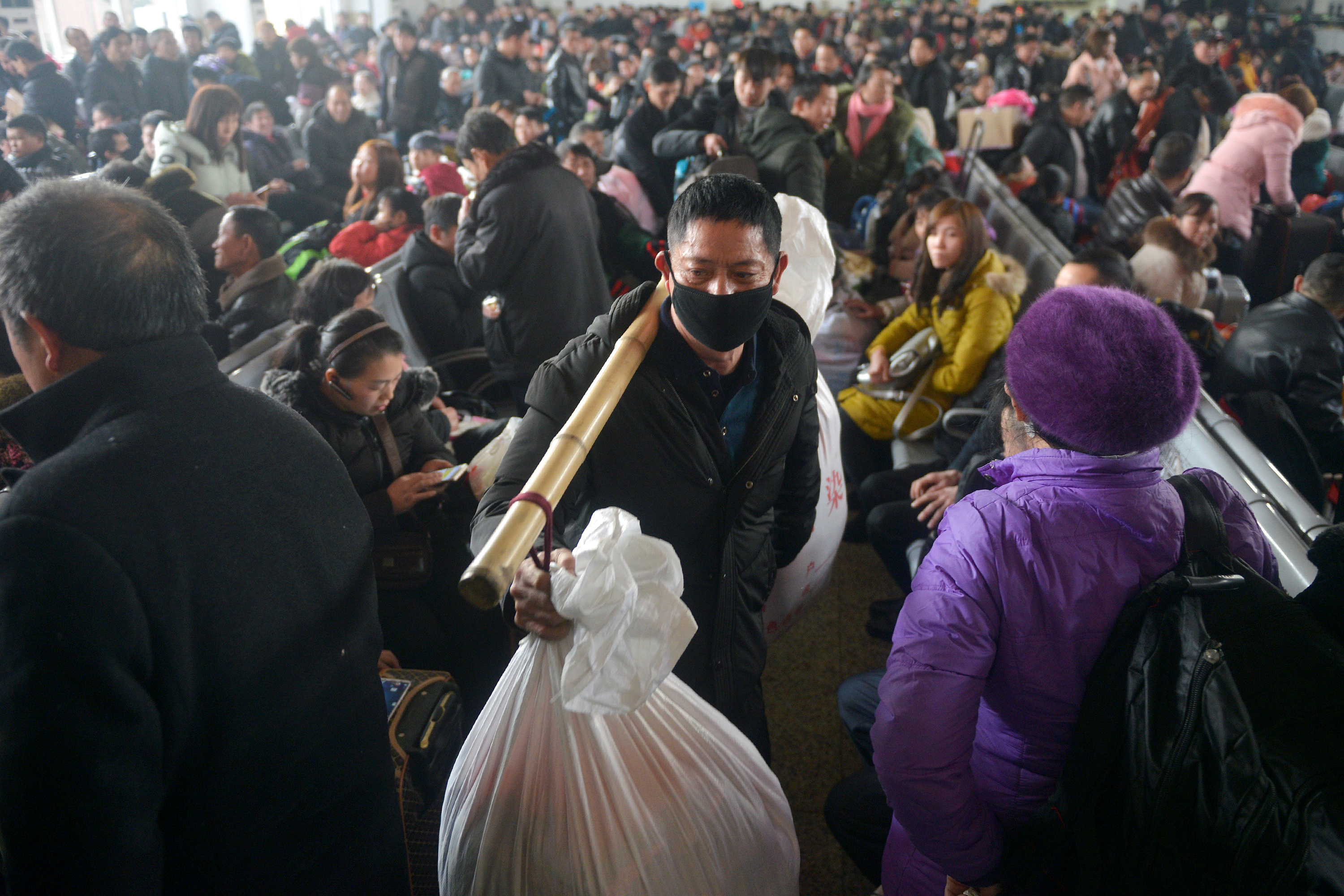 A man carries his belongings as he walks among passengers on the first day of the annual Spring Festival travel rush ahead of the Chinese Lunar New Year, at a railway station in Jiaxing, Zhejiang