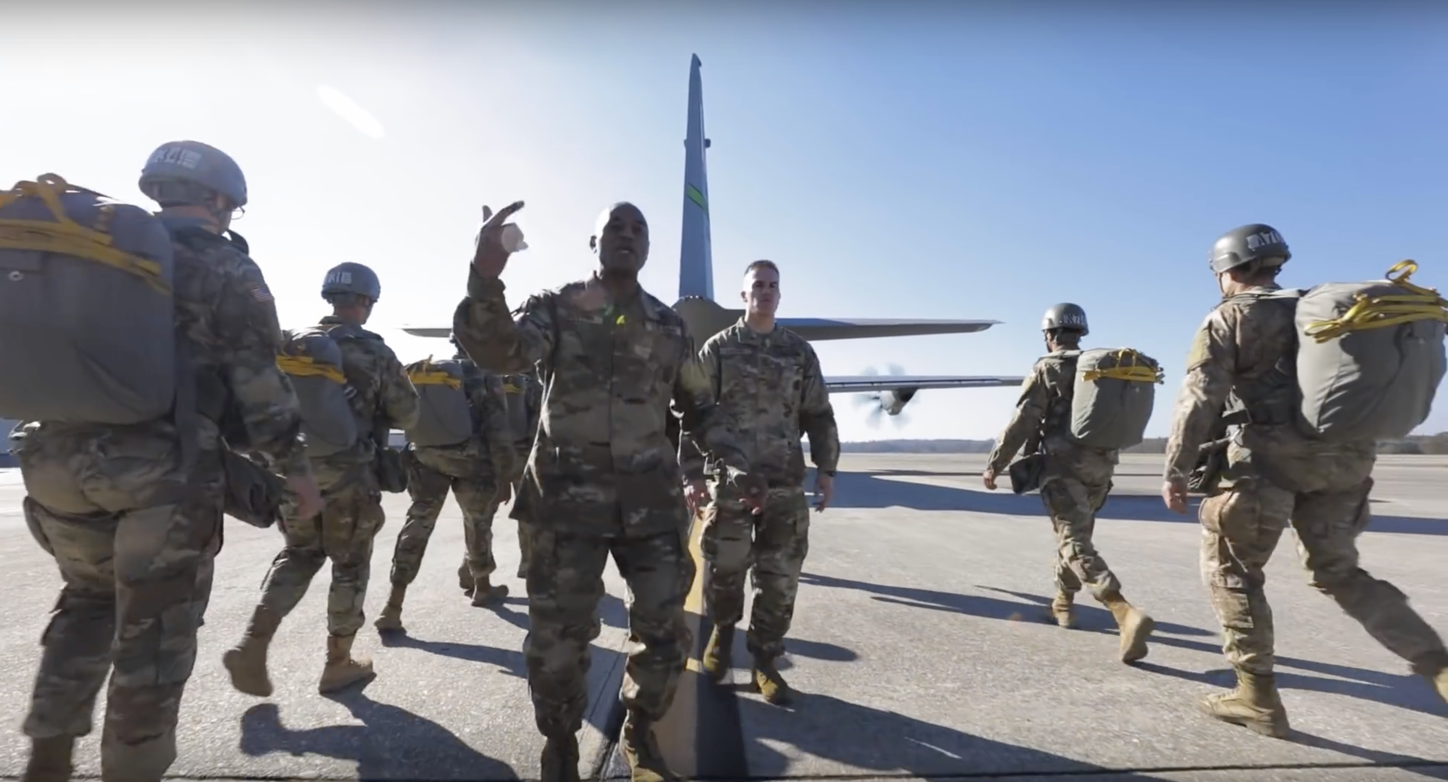 paratroopers walk to a plane behind two army men rapping to the camera