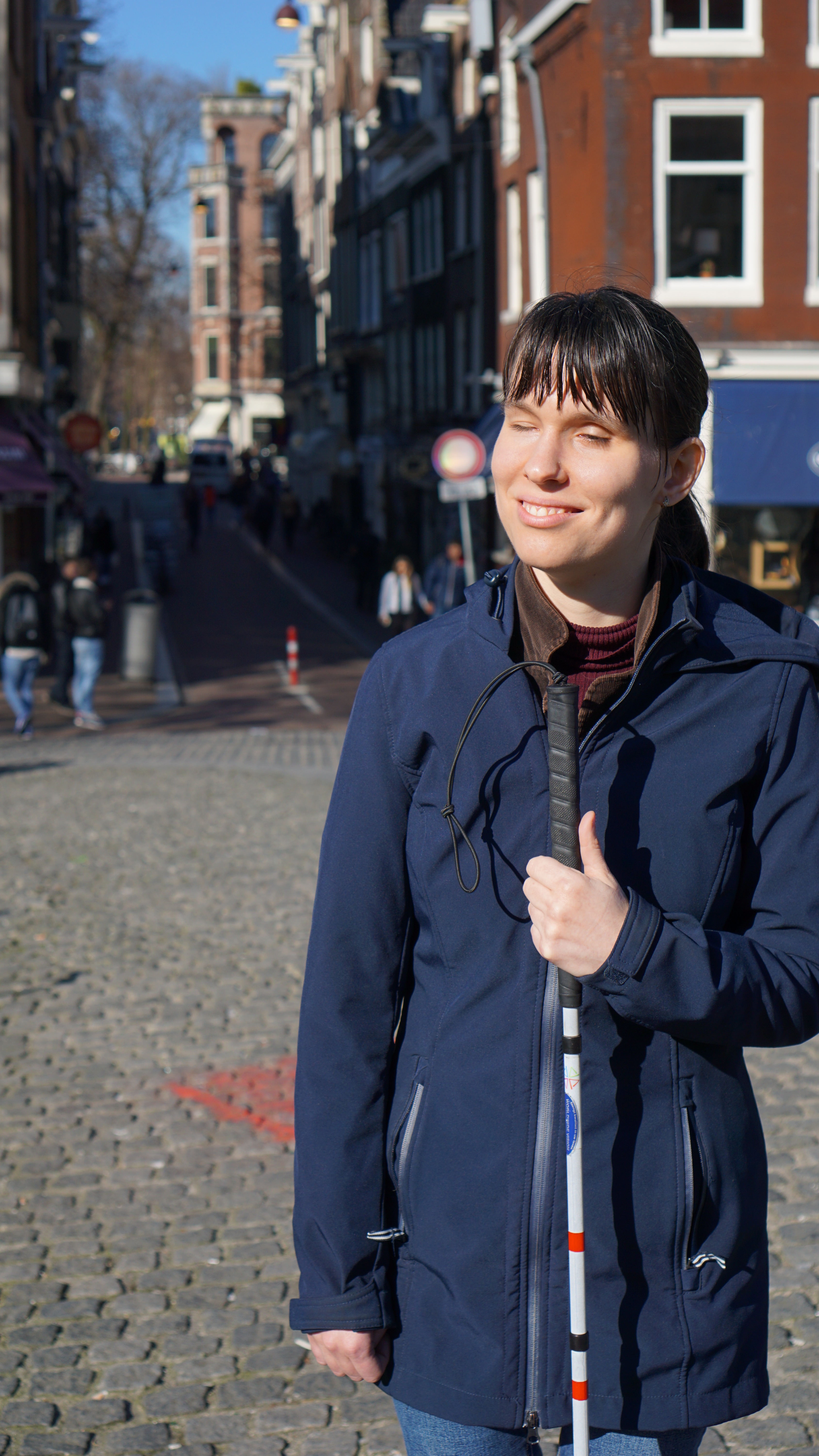 Slechtziende vrouw met blindegeleidestok en jas aan op een plein
