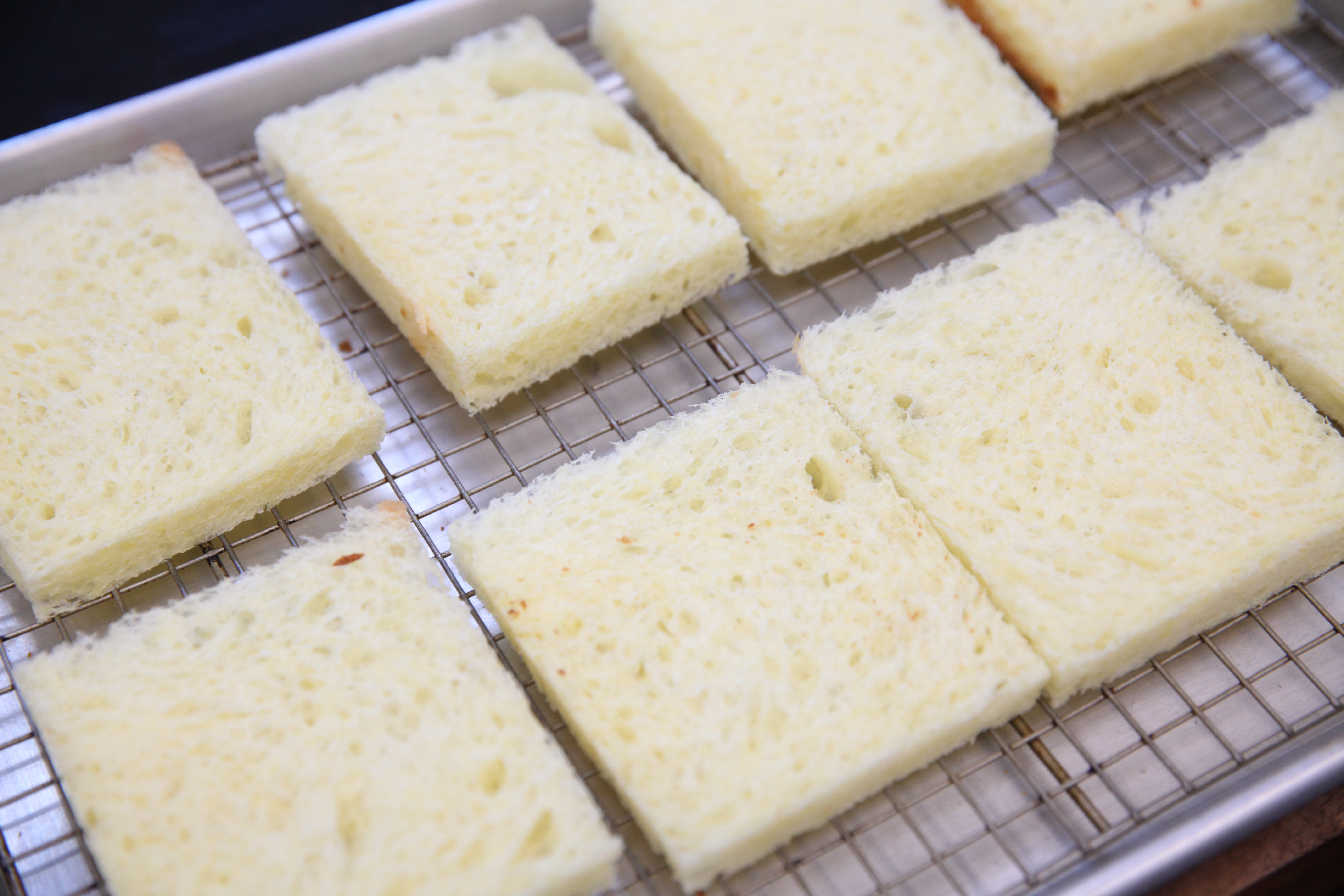 slices of white bread with the crusts cut off on a rack on a baking sheet