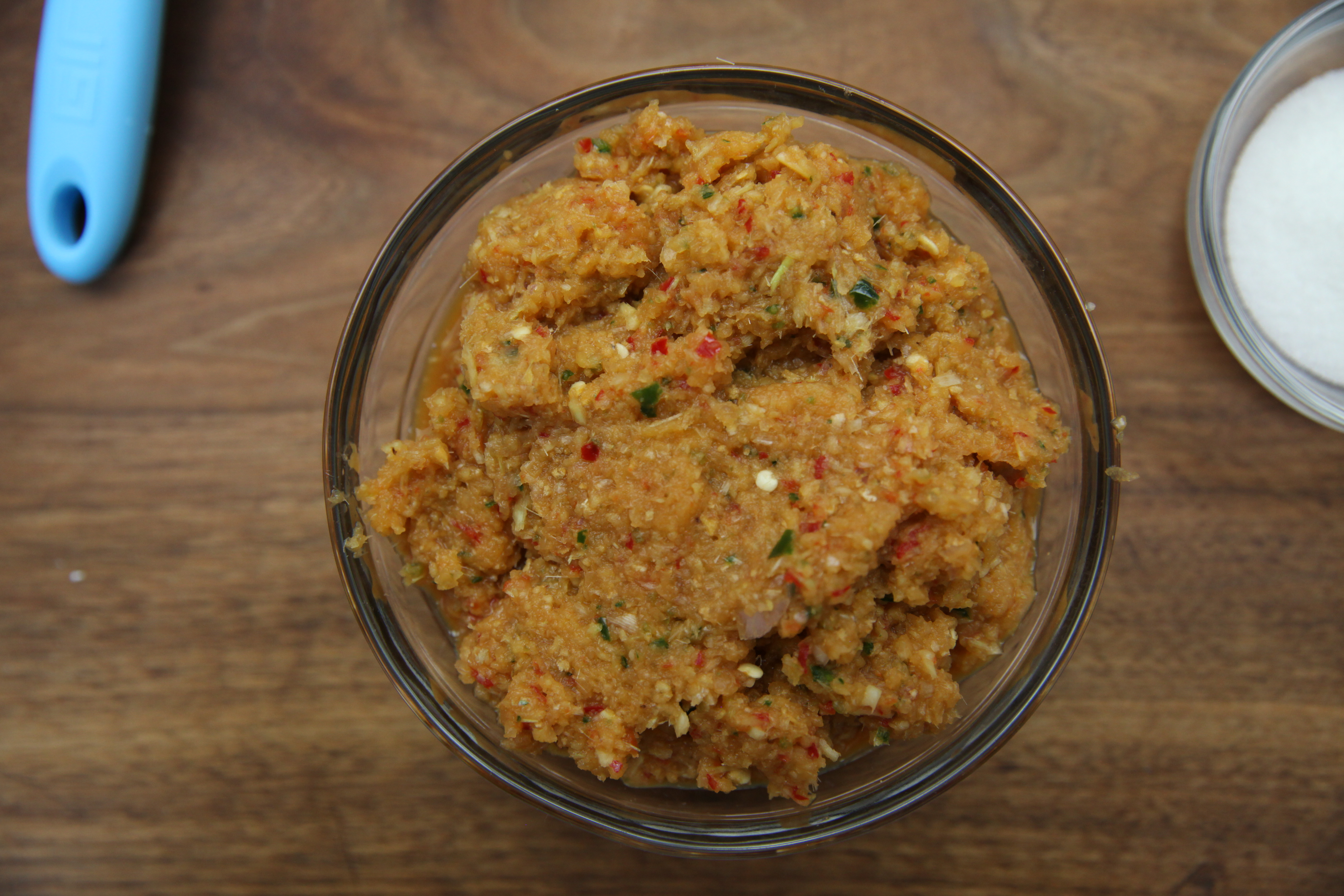 a bowl of curry paste with chiles, lemongrass, onions, shallots, and ginger in a glass bowl