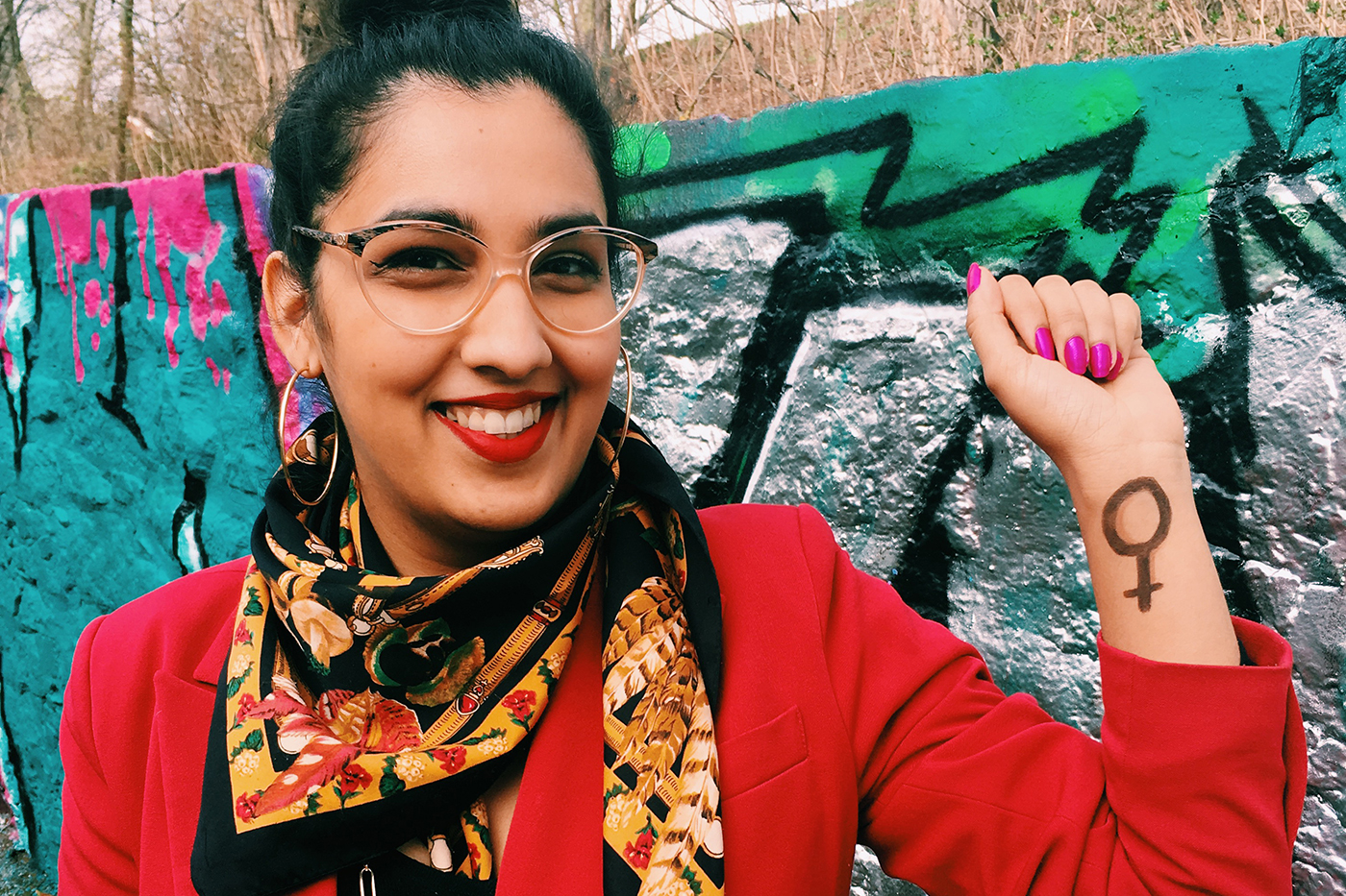 Amina Yousaf, die Faust reckend, vor einer Wand