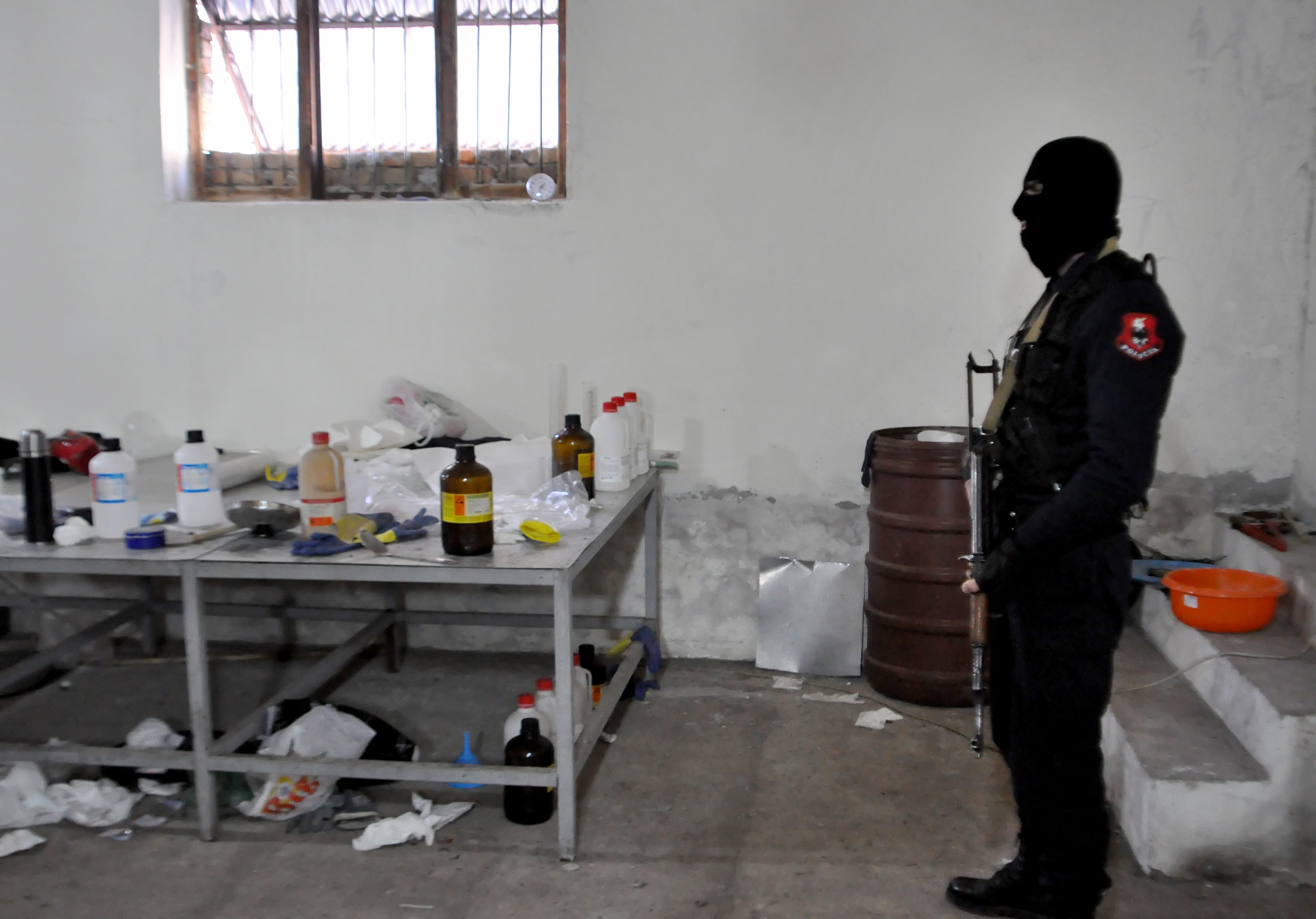 A masked Albanian police officer searches a clandestine cocaine refining laboratory in 2015.