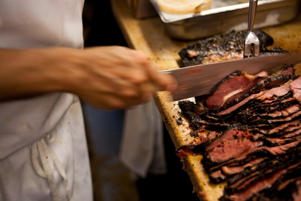 the hand of a cook at katz's delicatessen slicing a piece of meat