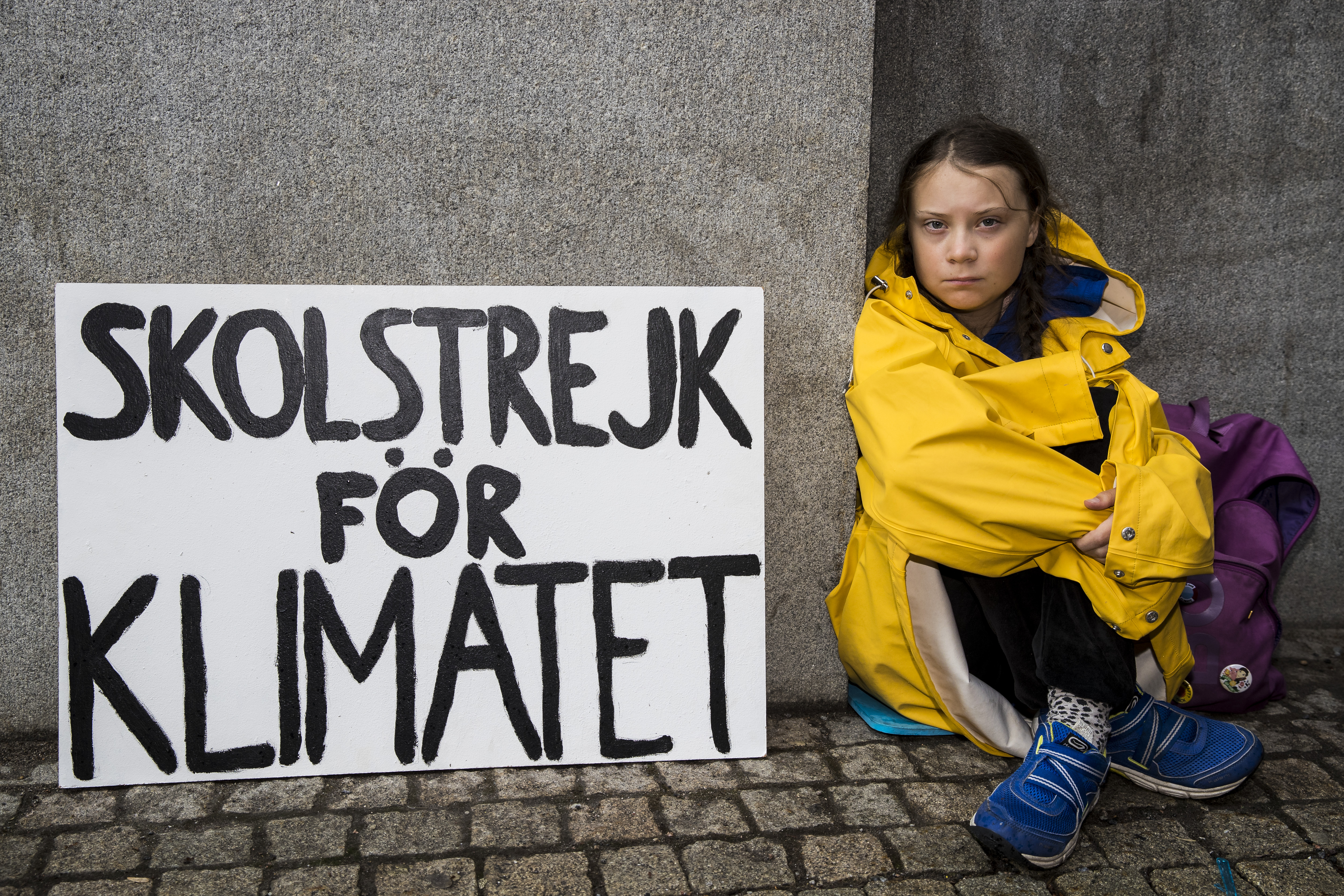 Greta Thunberg sitting on the ground next to a protest sign