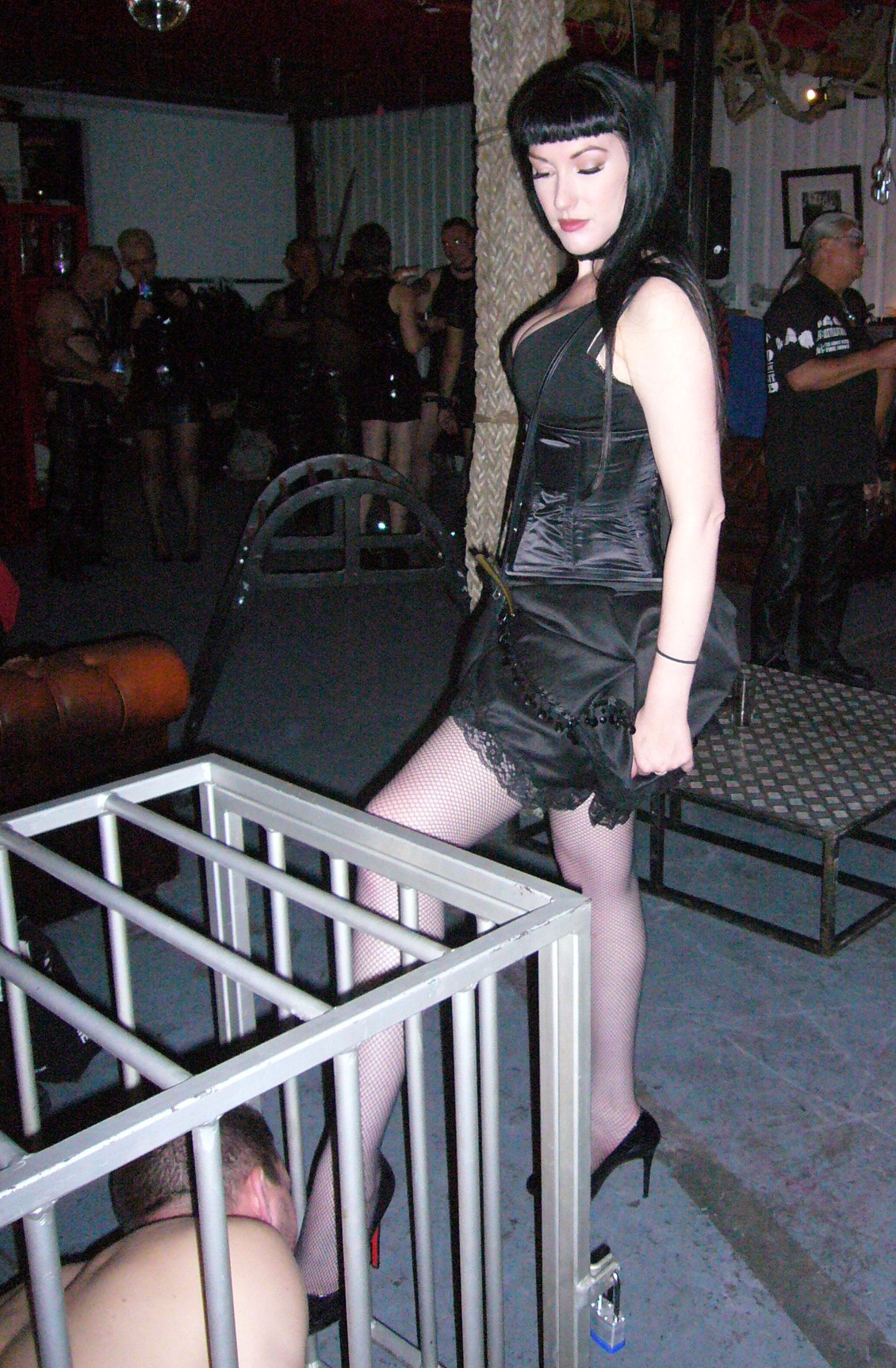 Professional dominatrix Mistress Cleo with a slave in a cage licking her foot