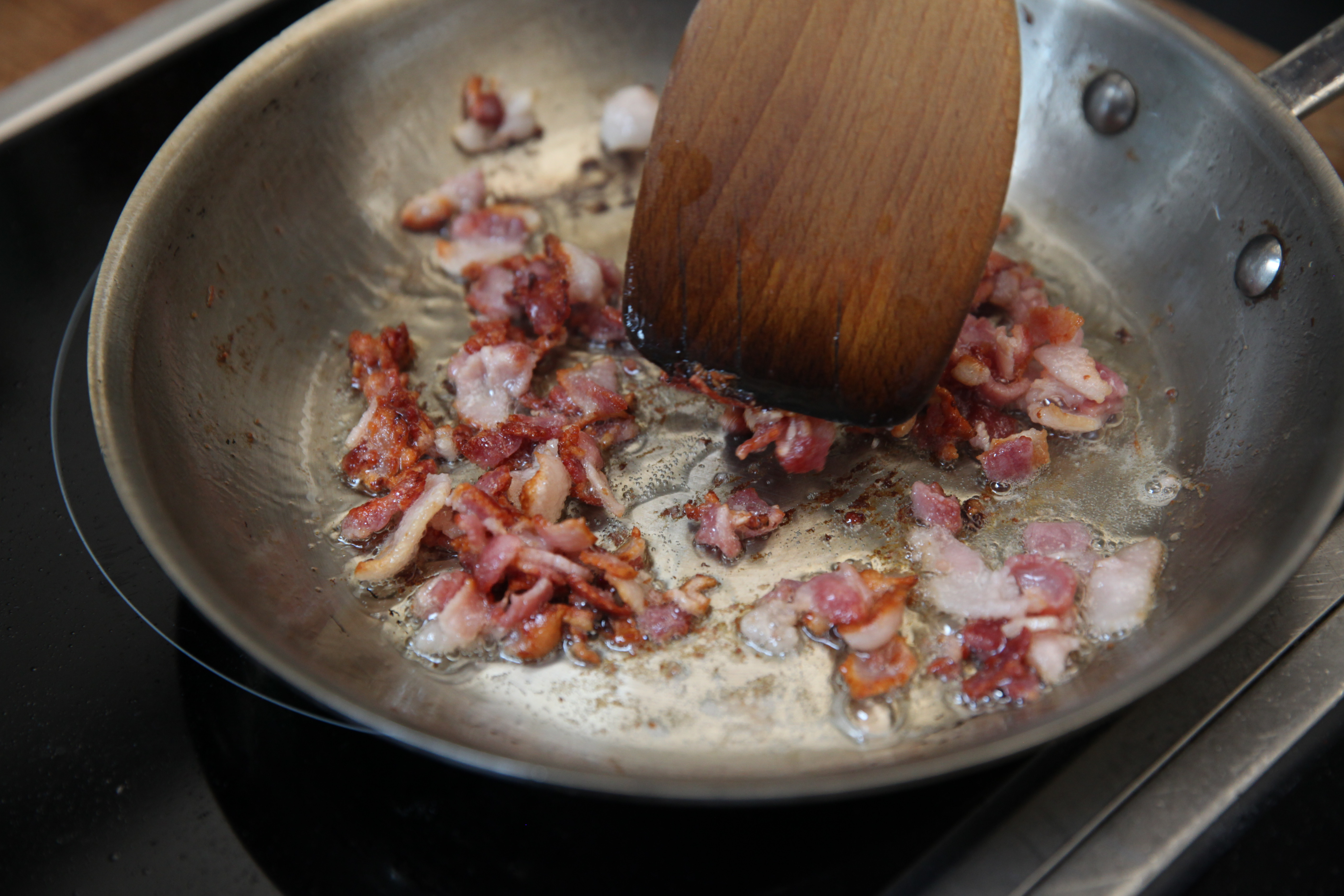 bacon bits cooking in a stainless steel pan in the munchies test kitchen