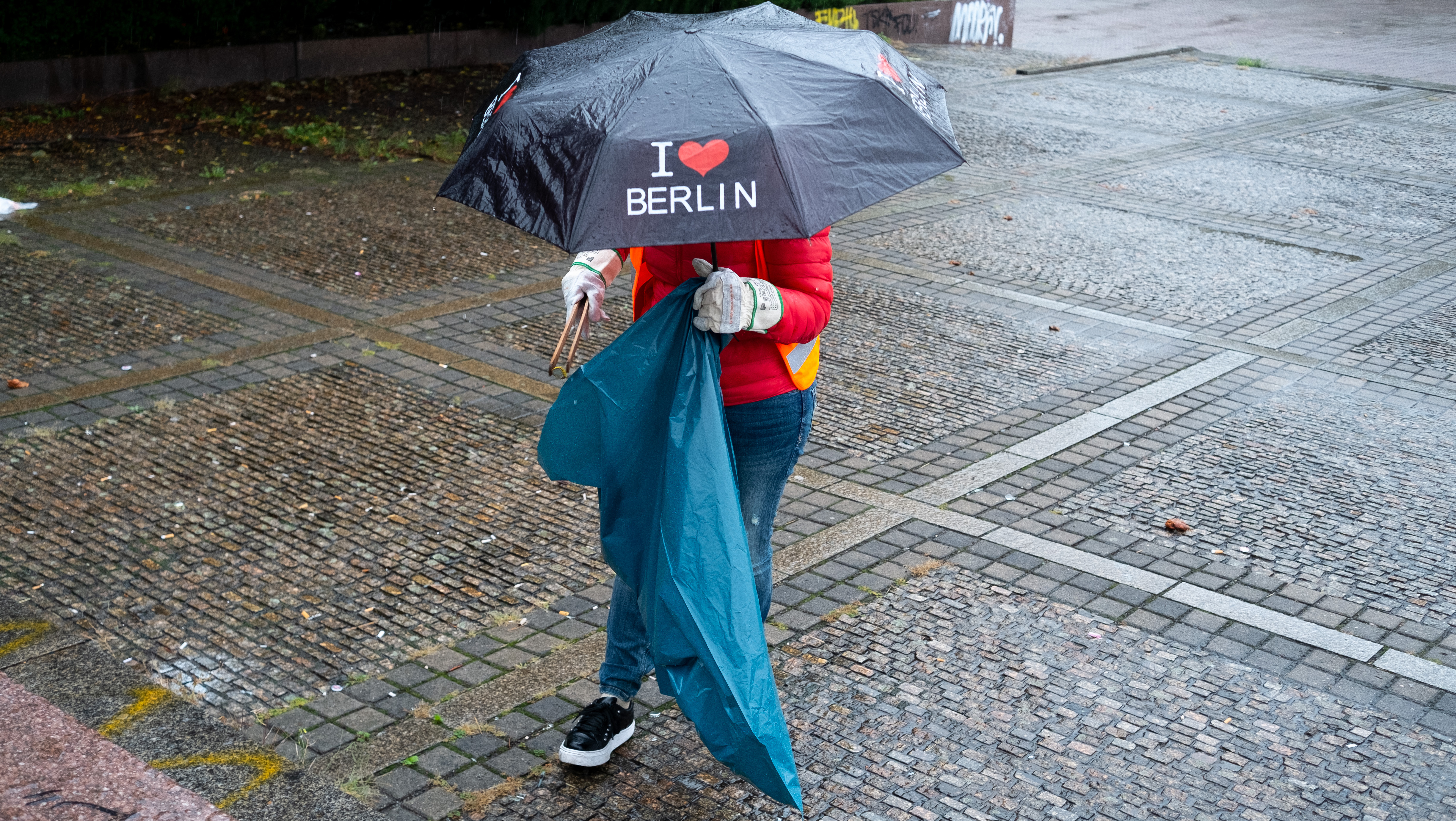 Eine Person trägt einen Regenschirm und sammelt Müll