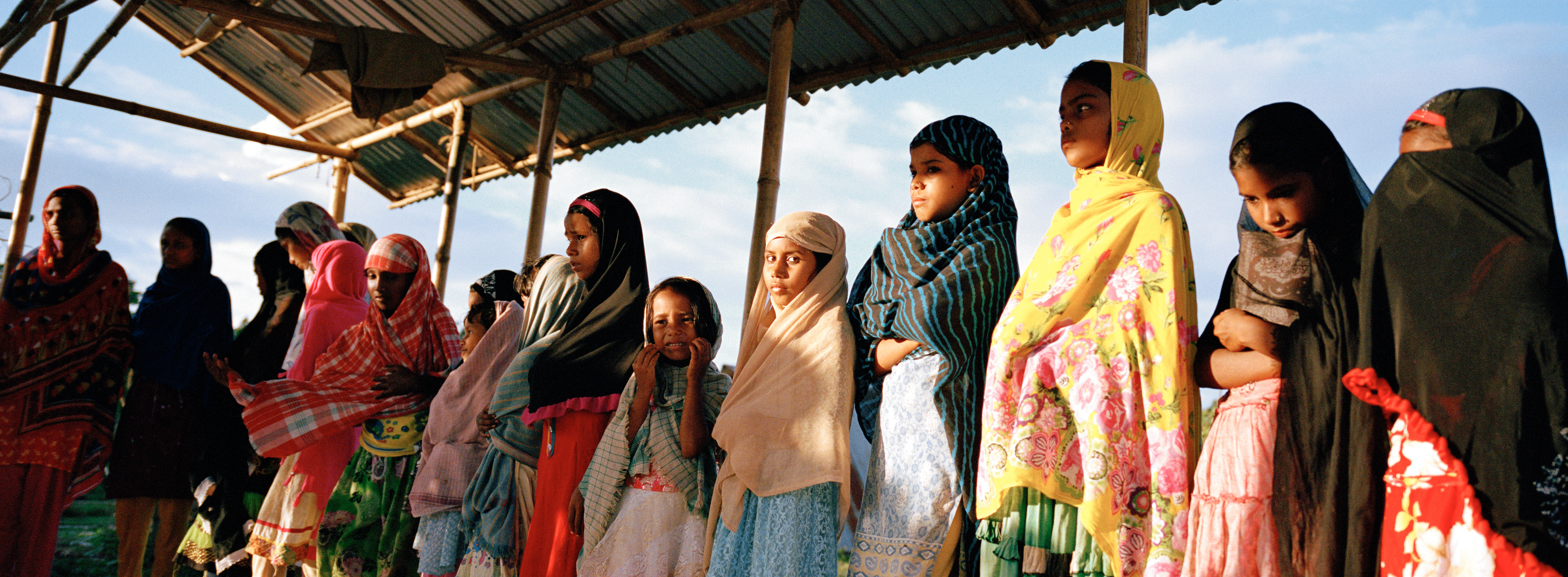 Young women, uprooted by river erosion and presently living in a camp for displaced persons, sing hymns at a widely-attended after-school program. The program is the only opportunity for people in the camp to practice Islam as a community.