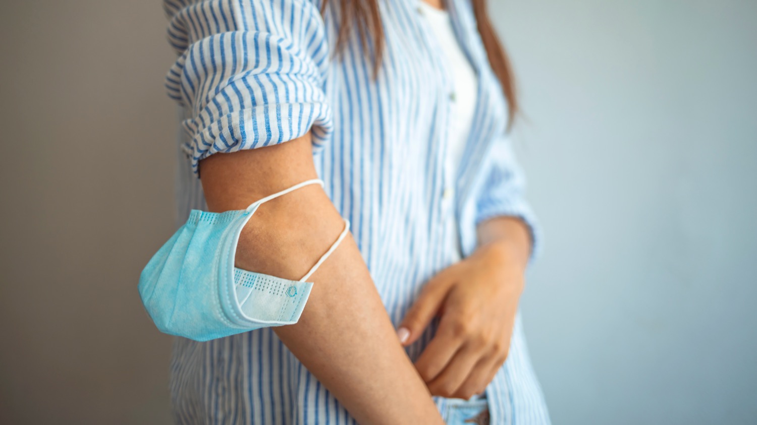 Woman showing the wrong way to wear a face mask as protection against the spread of the coronavirus or Covid-19 as she puts it around her upper arm in a useless gesture