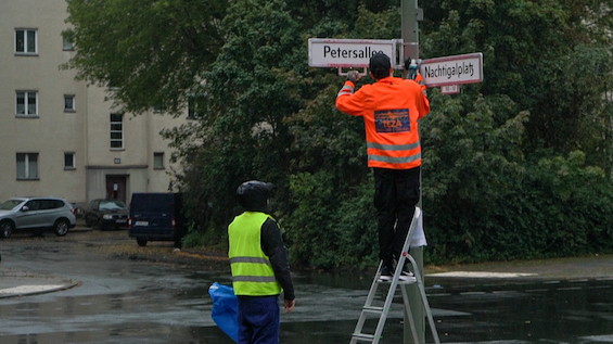 Rocco und seine Brüder. Two men in high visibility vests taking down a street sign.