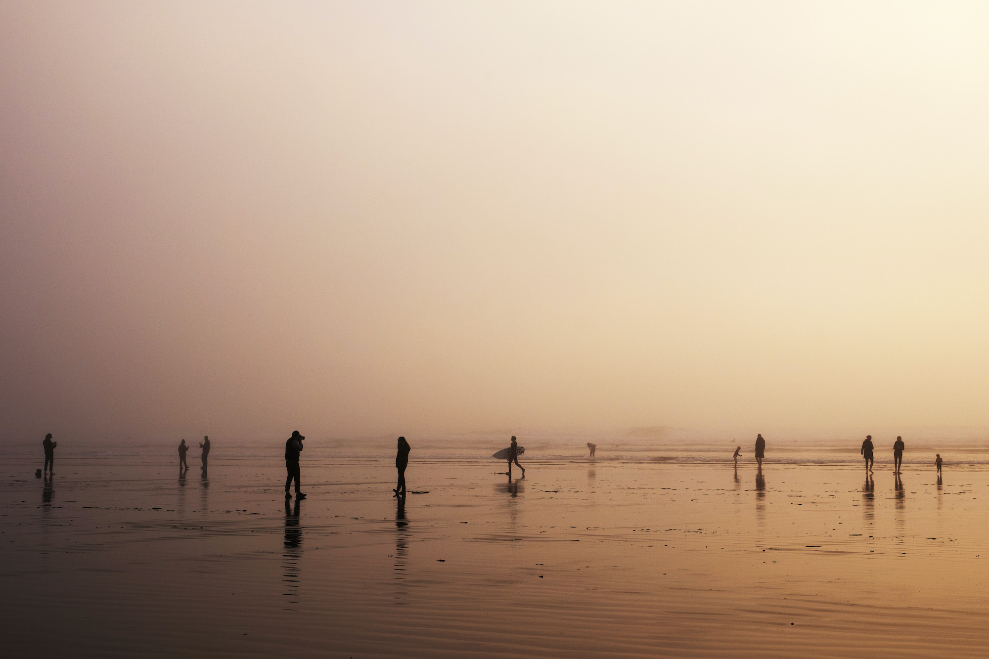 People walk along Cox Bay Beach in Tofino at sunset