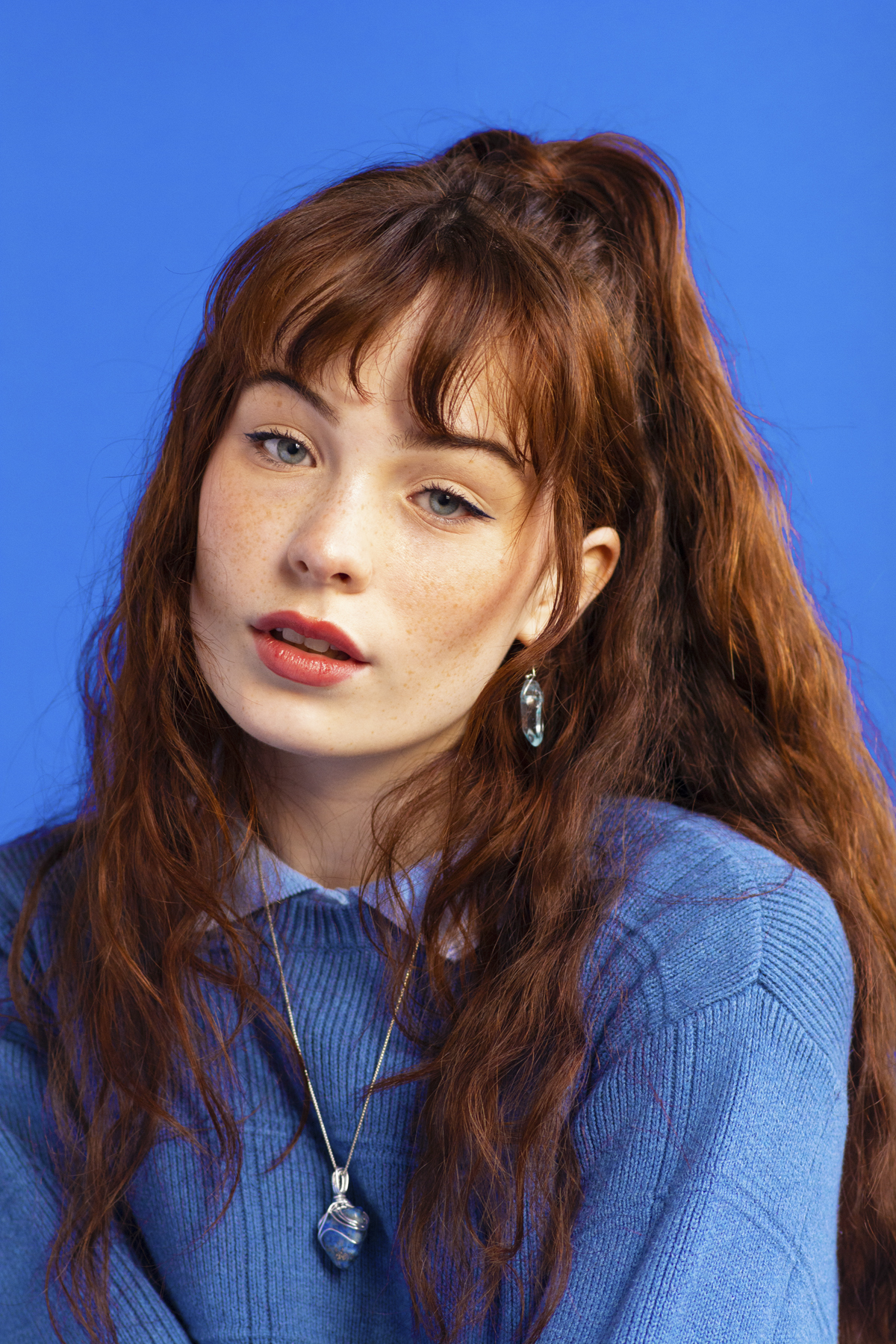 Woman with a blue shirt, blue jumper and stone necklace. Photographed by Marcus Branch.