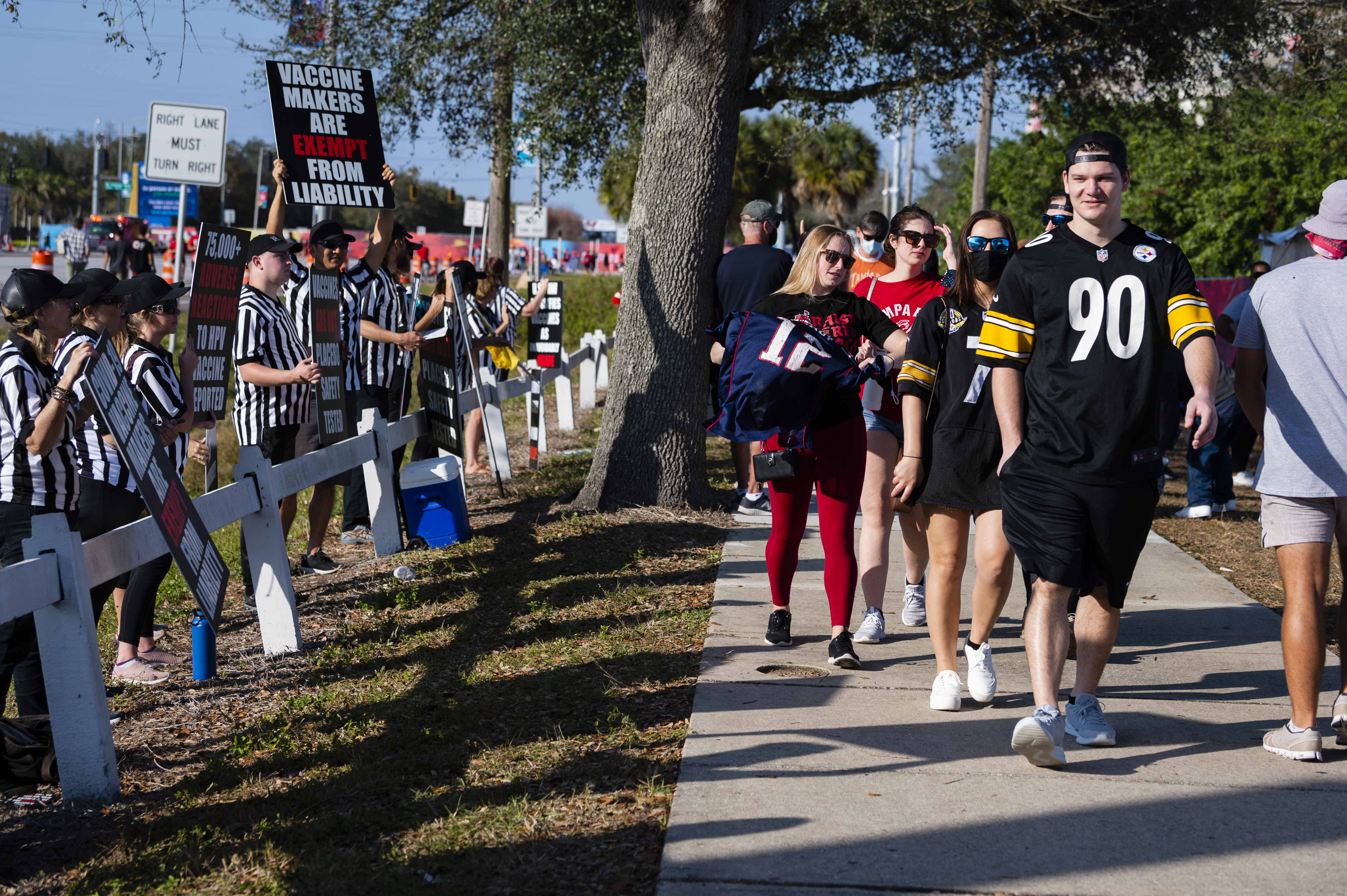 Fans pass by a protest against Covid-19 vaccine outside the Raymond James Stadium ahead of the Super Bowl LV game between Tampa Bay Buccaneers and Kansas City Chiefs in Tampa, Florida, United States on February 07, 2021.