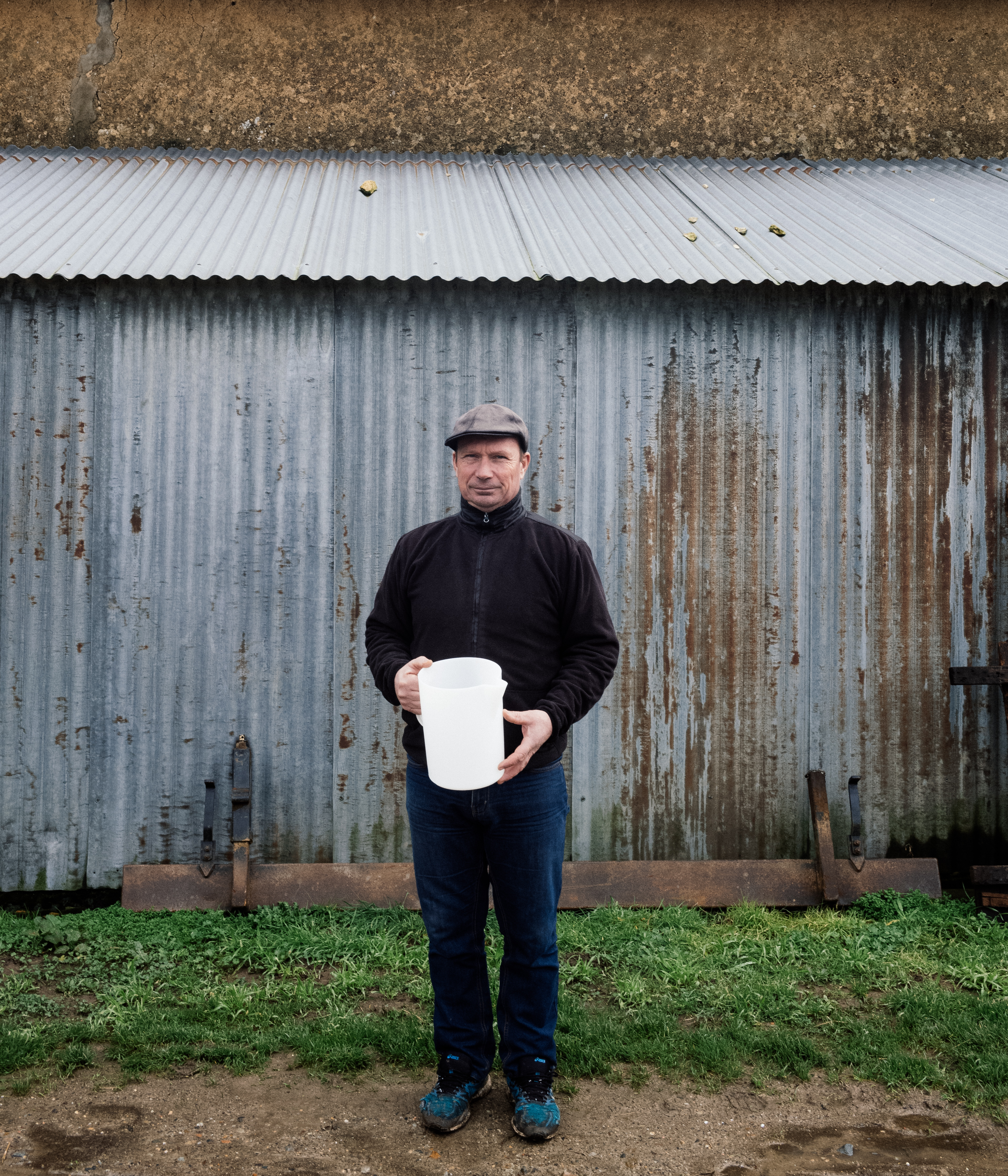Patrice Riauté – man with no facial hair, wearing a cap, a black fleece jacket and jeans, holding a large plastic jug.