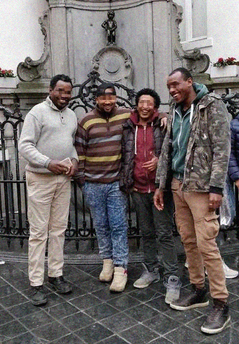 Vier Geflüchtete posieren fröhlich vor einem Brüsseler Wahrzeichen