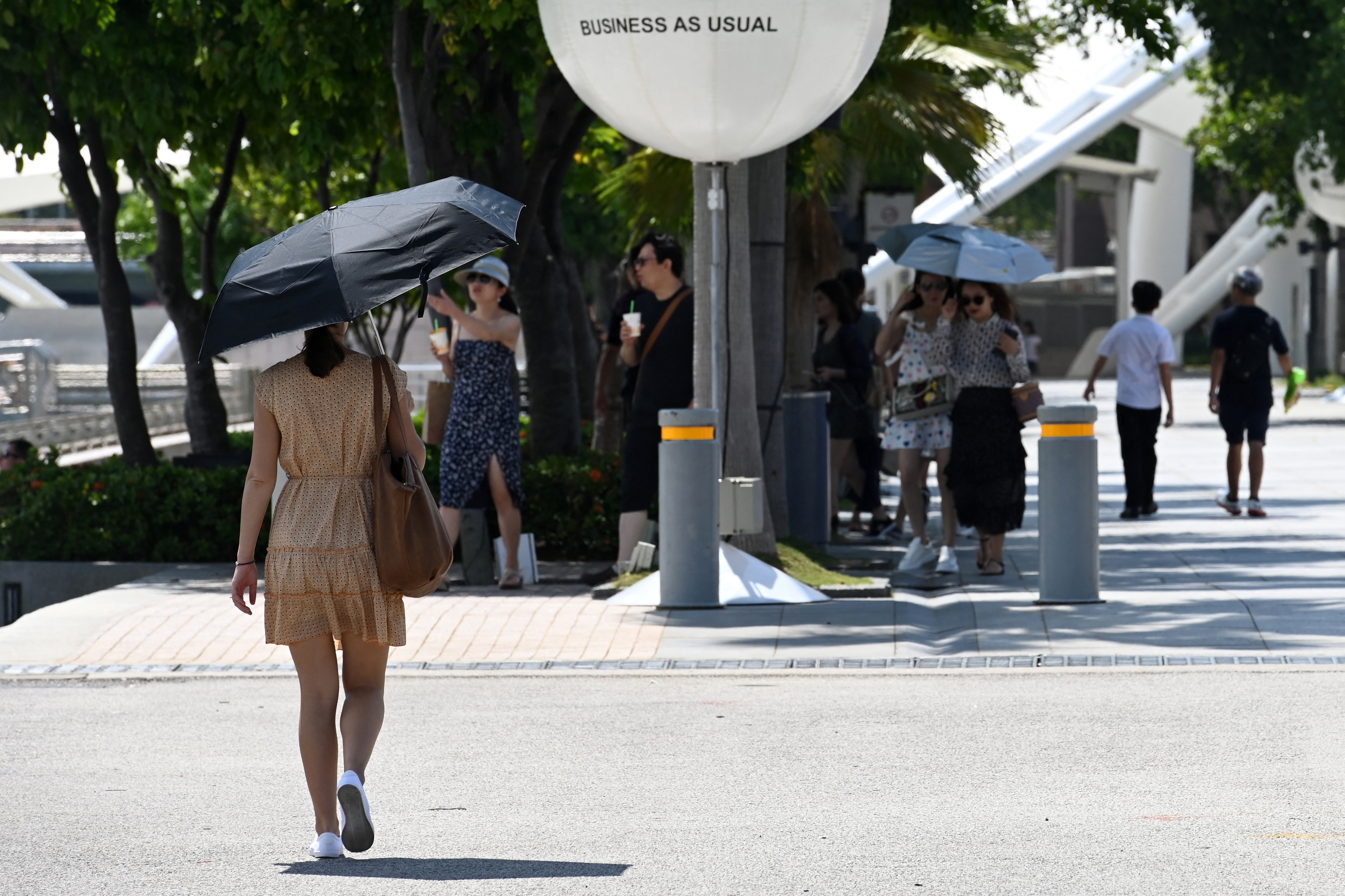 People shield themselves from the sun as they walk along Marina Bay in Singapore. (PHOTO: AFP / ROSLAN RAHMAN)