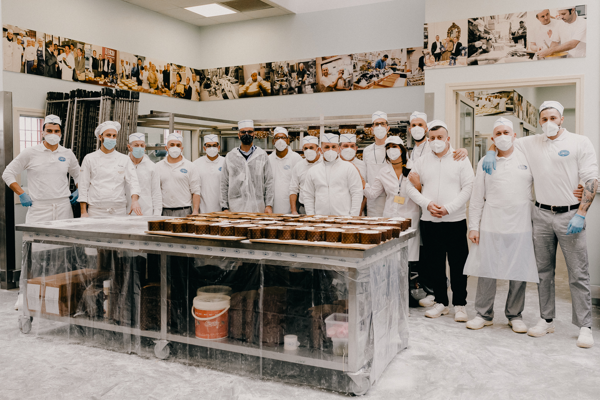 Giotto Bakery – A group picture of 15 men and one woman, standing side by side and hugging
